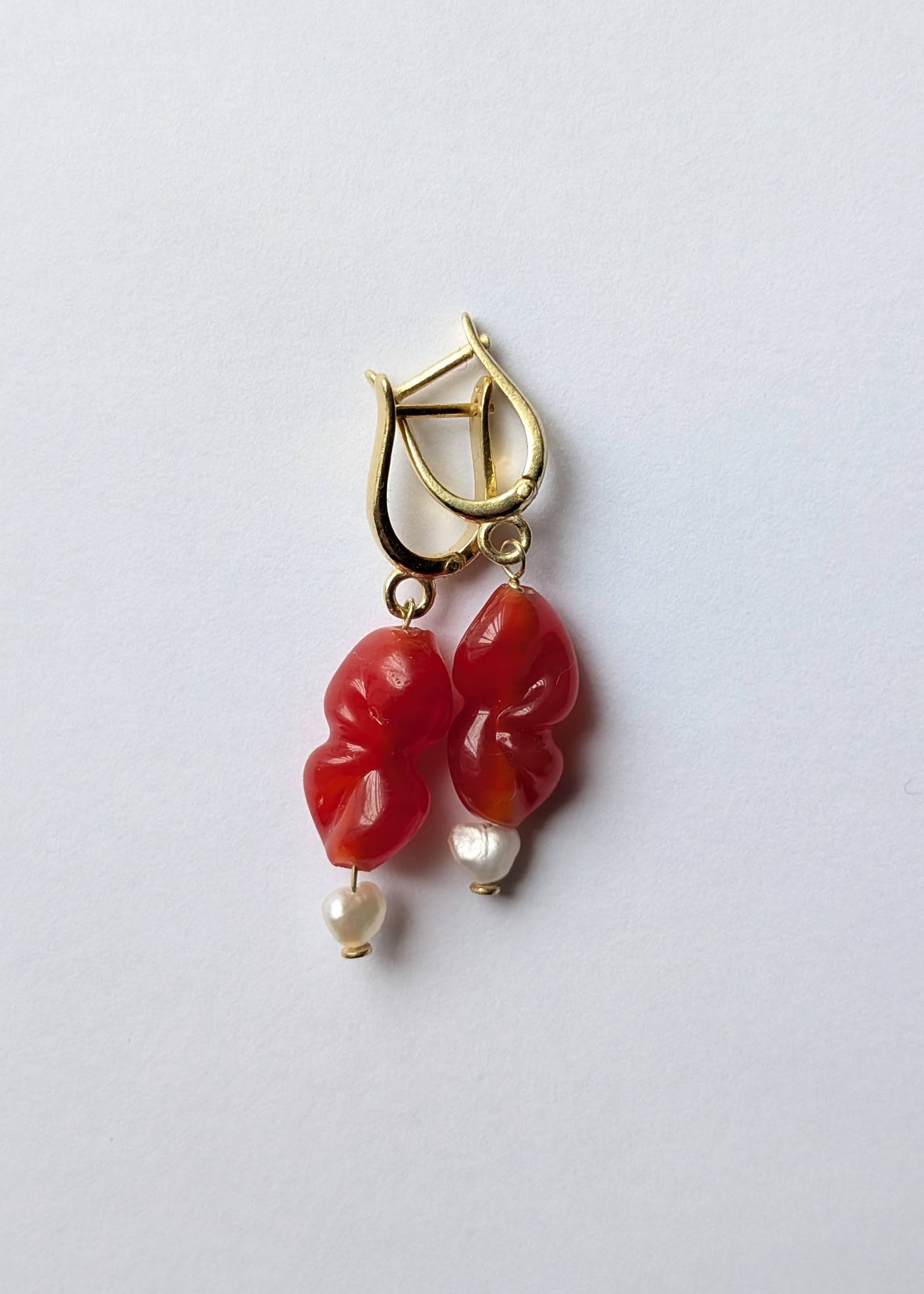 Gold earring with red stones and pearl-like beads on a light gray background