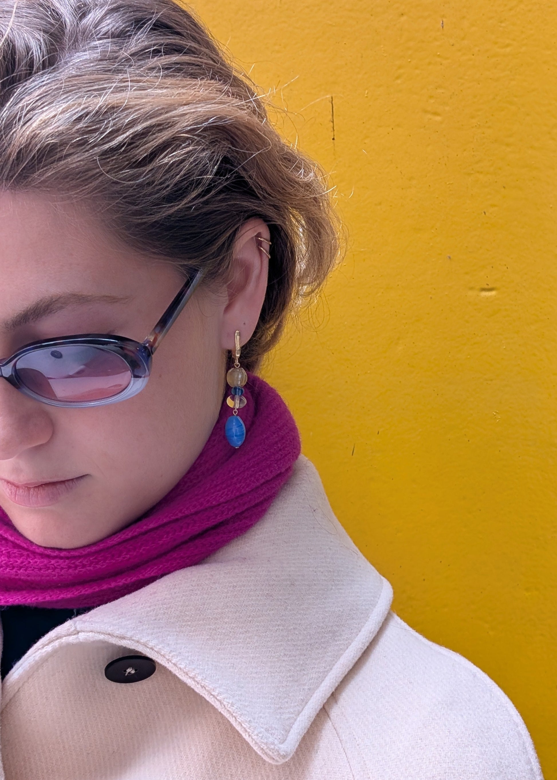 Person wearing a pink scarf and sunglasses against a yellow wall