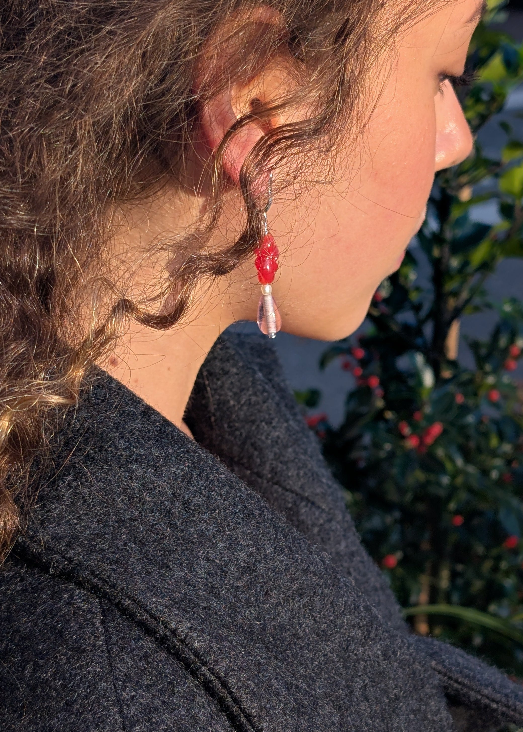Close-up of a person wearing red earrings with a blurred natural background