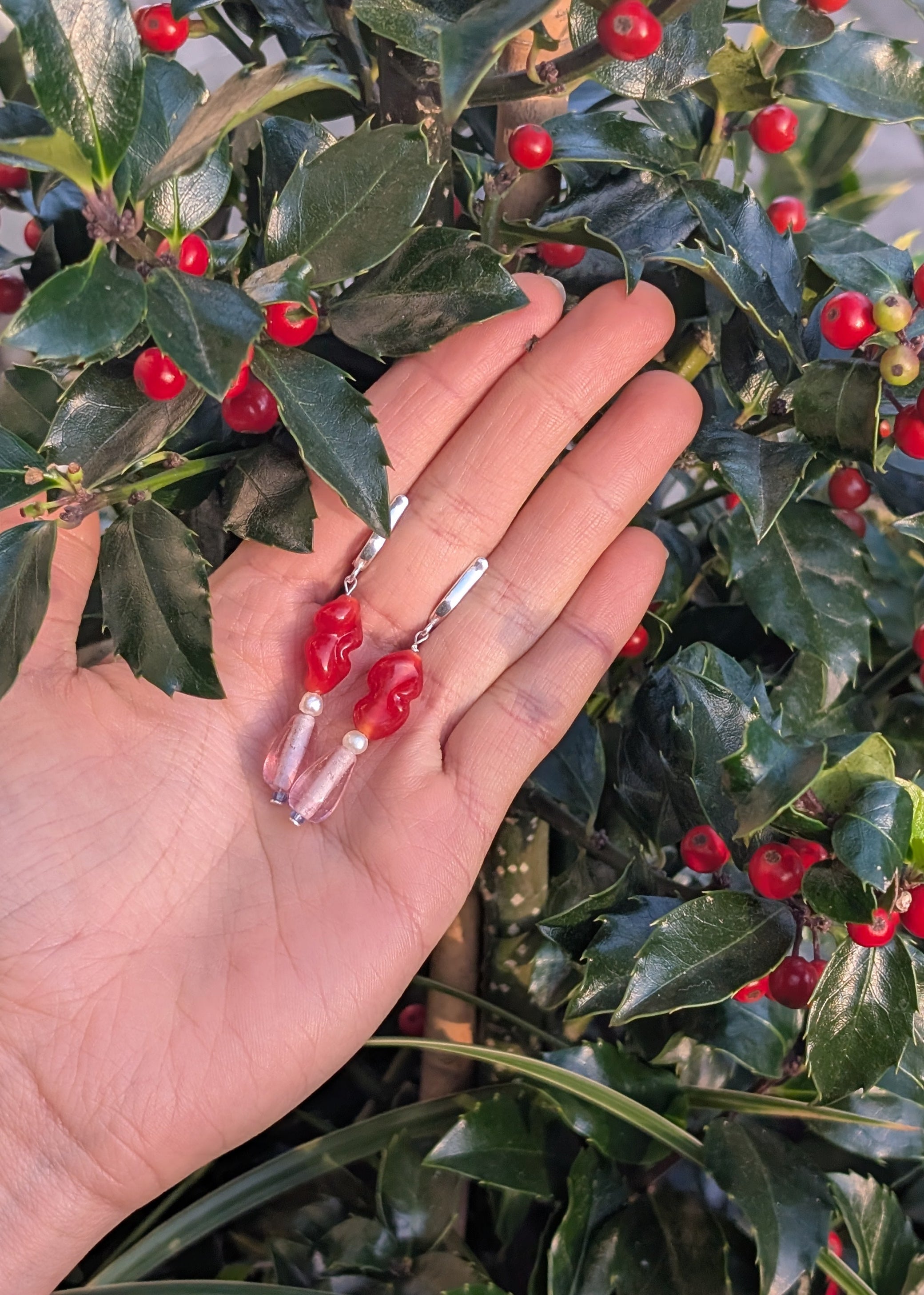 Hand with a ring held against a background of green leaves and red berries