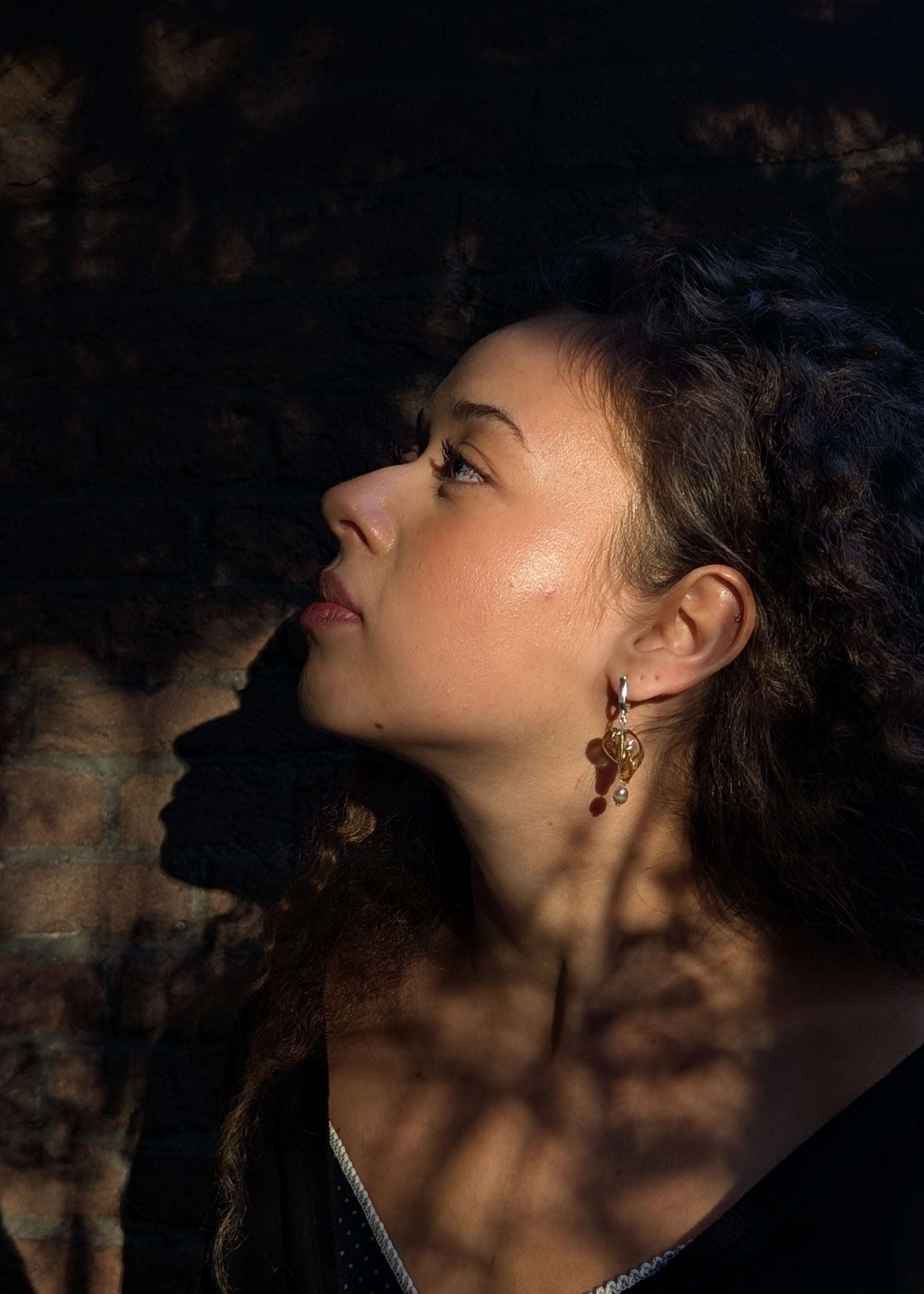 Woman with dark hair and earrings looking upwards in a dimly lit setting