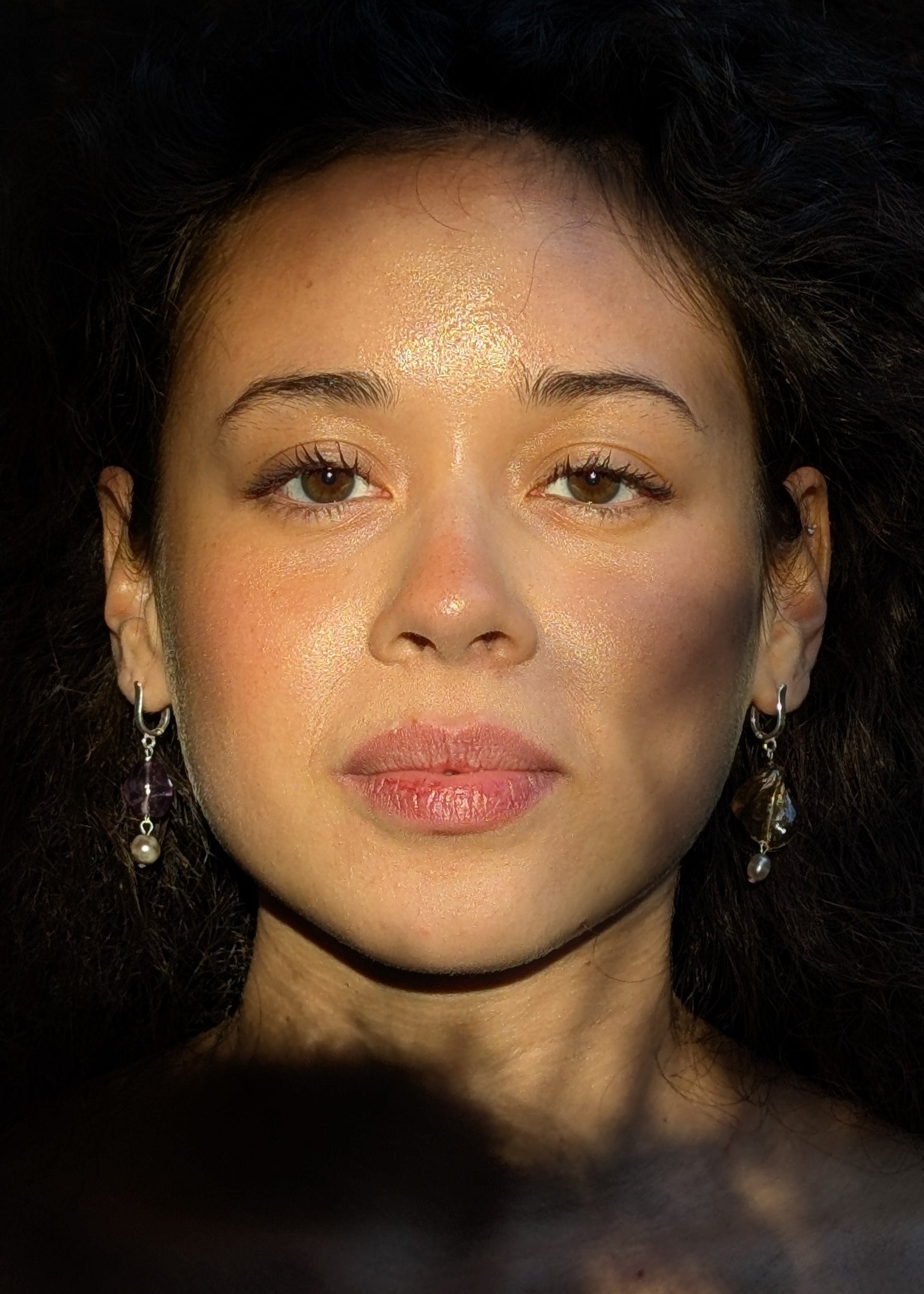 Close-up of a person with dark hair and earrings against a dark background