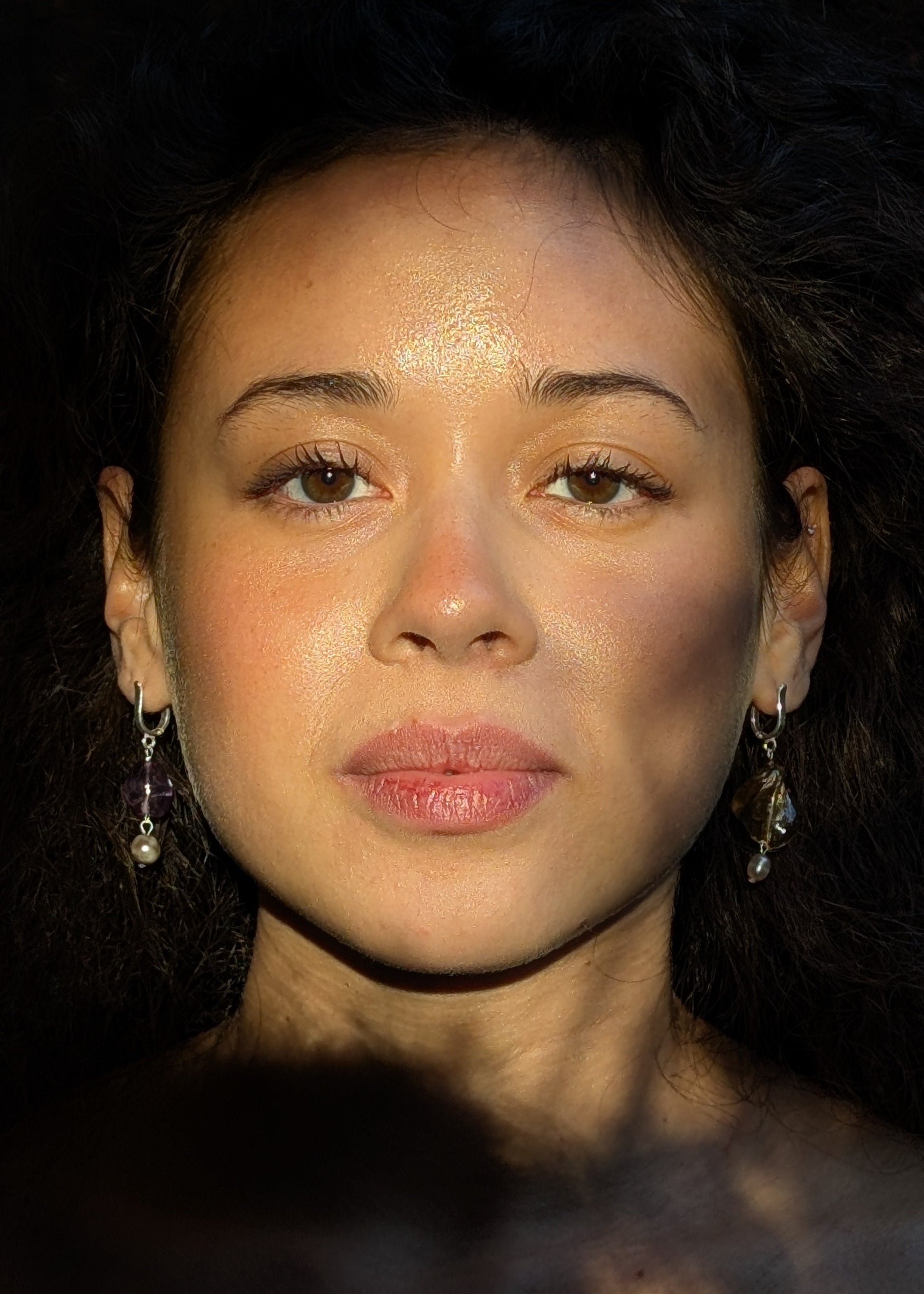 Close-up of a person with dark hair and earrings against a dark background