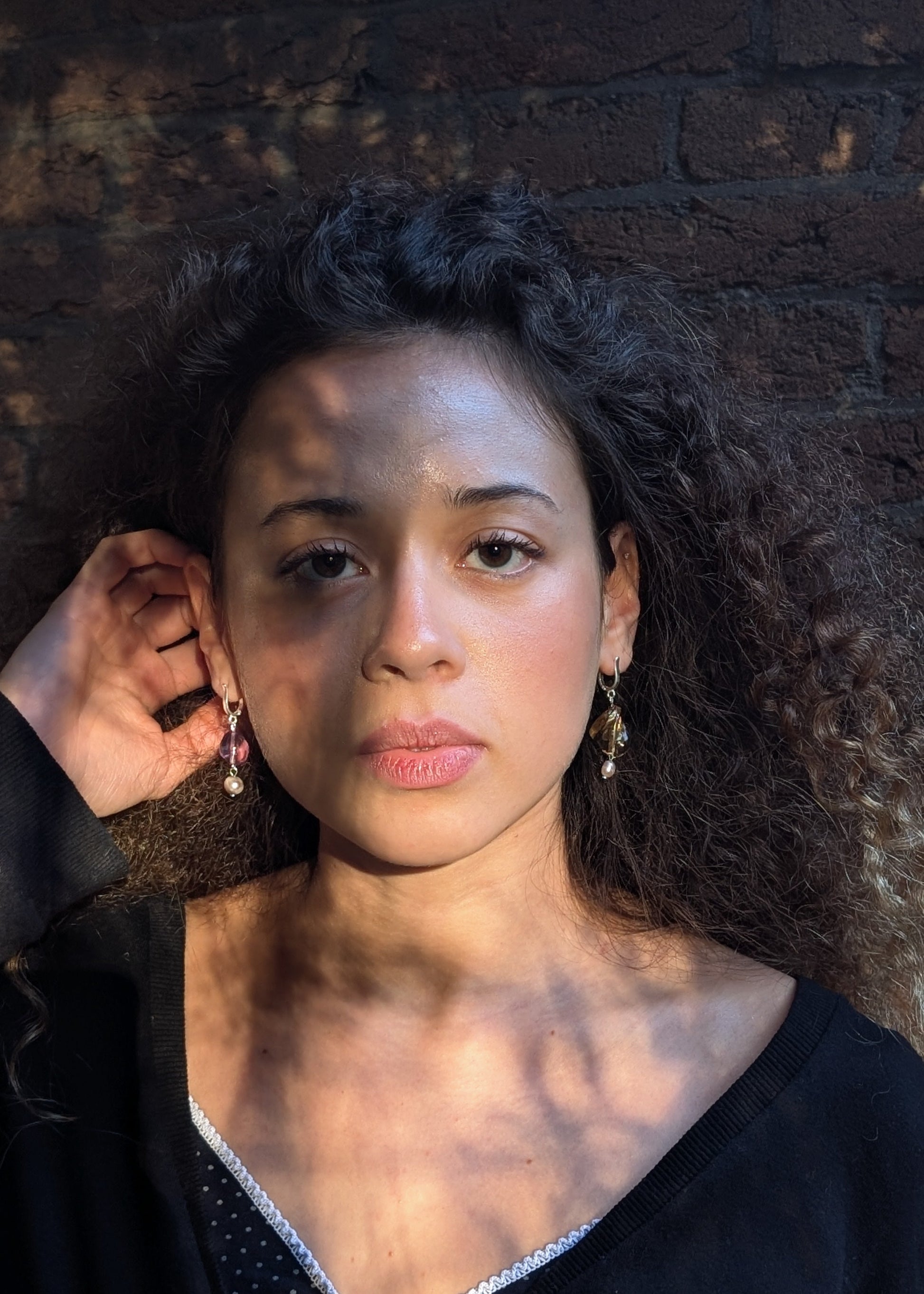 Woman with dark hair and earrings against a textured wall