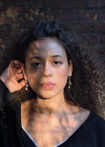 Woman with dark hair and earrings against a textured wall