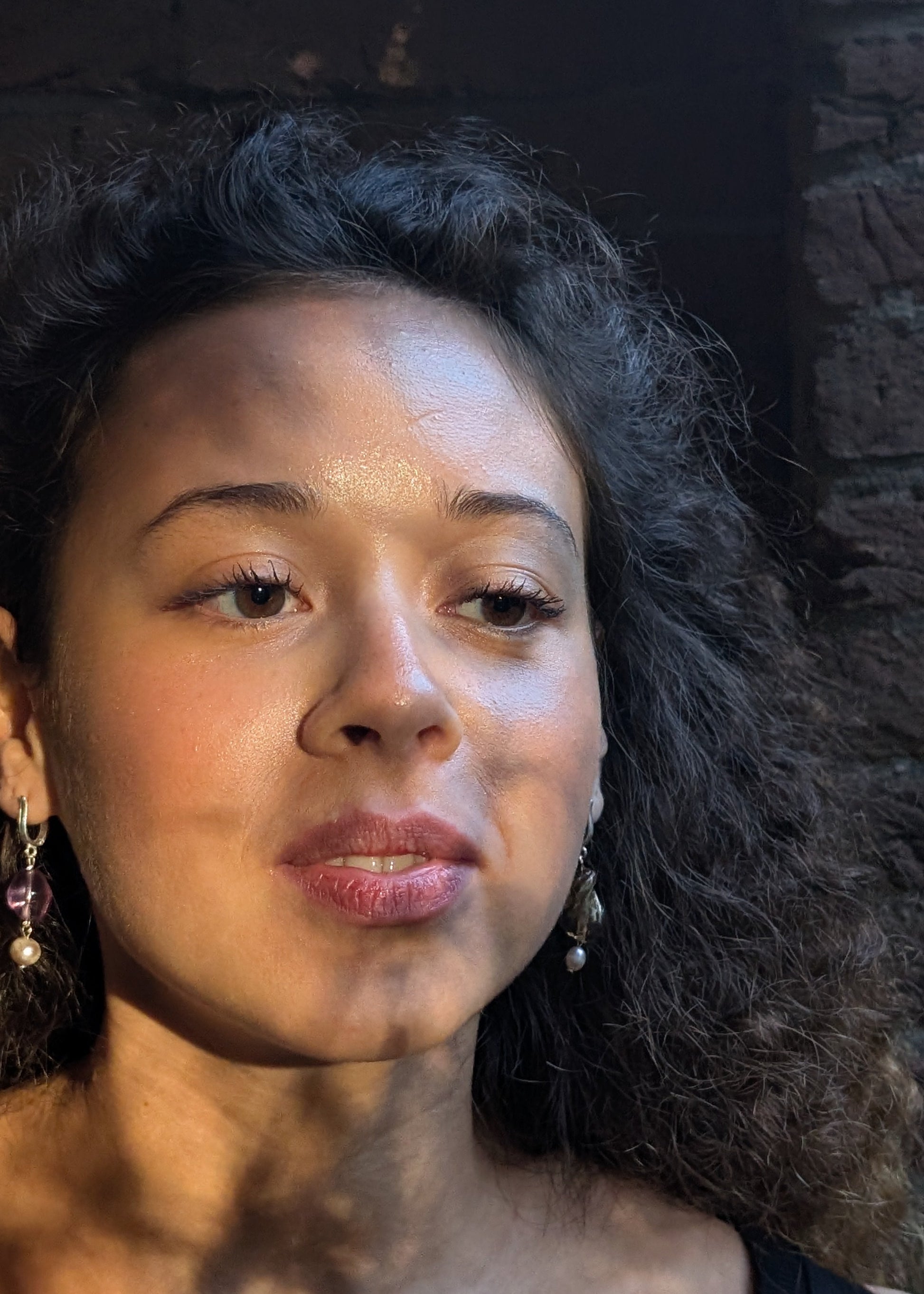 Woman with dark hair and earrings against a dark background