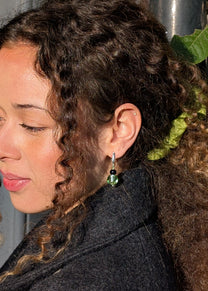 Close-up of a person with curly hair and green earrings, wearing a dark coat.