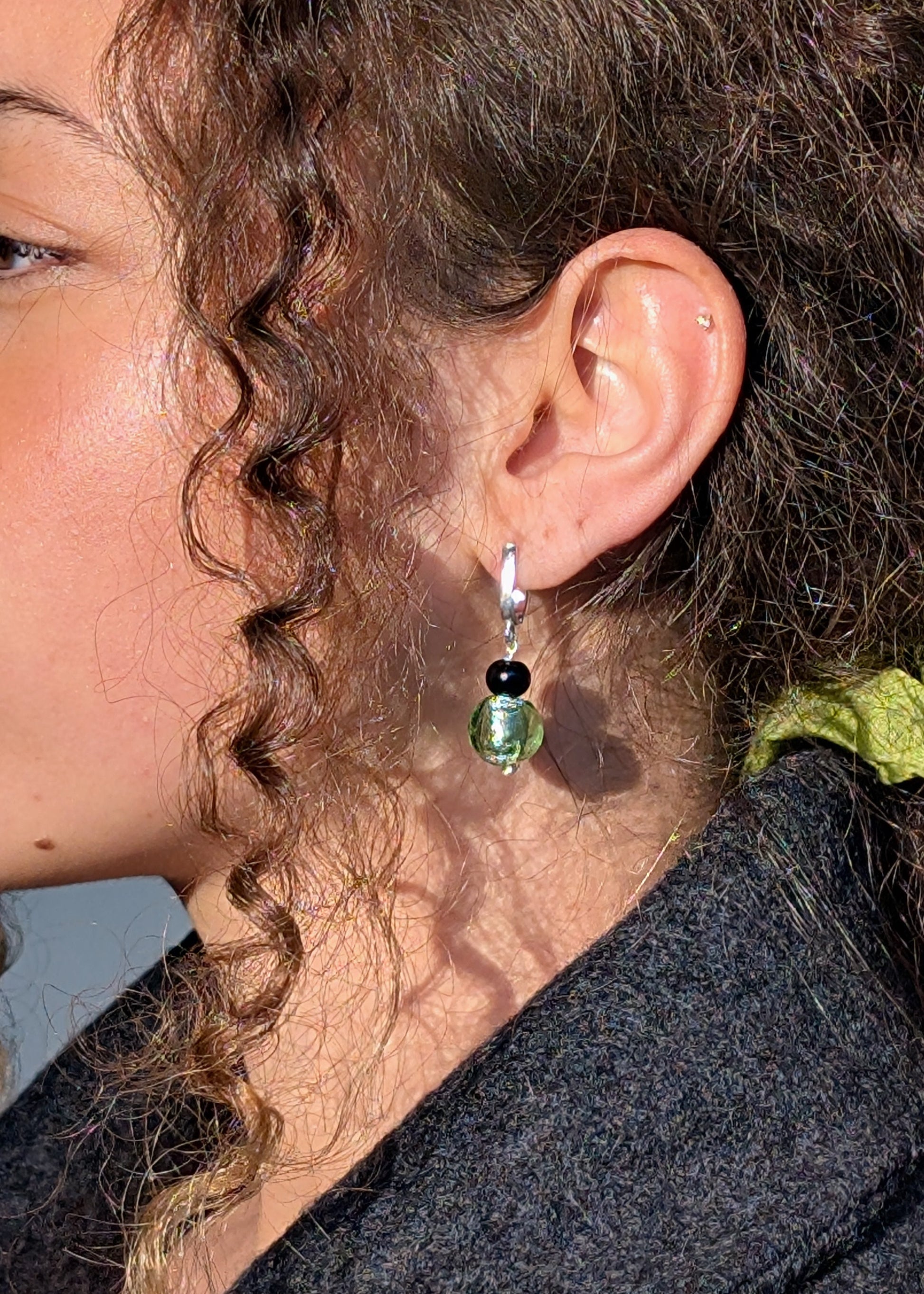 Close-up of a person wearing a green earring with a black bead.