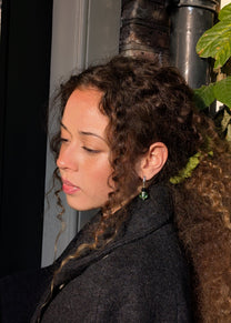 Woman with curly hair wearing a dark coat, standing indoors.