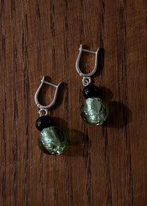 Pair of earrings with green beads and silver hooks on a wooden surface