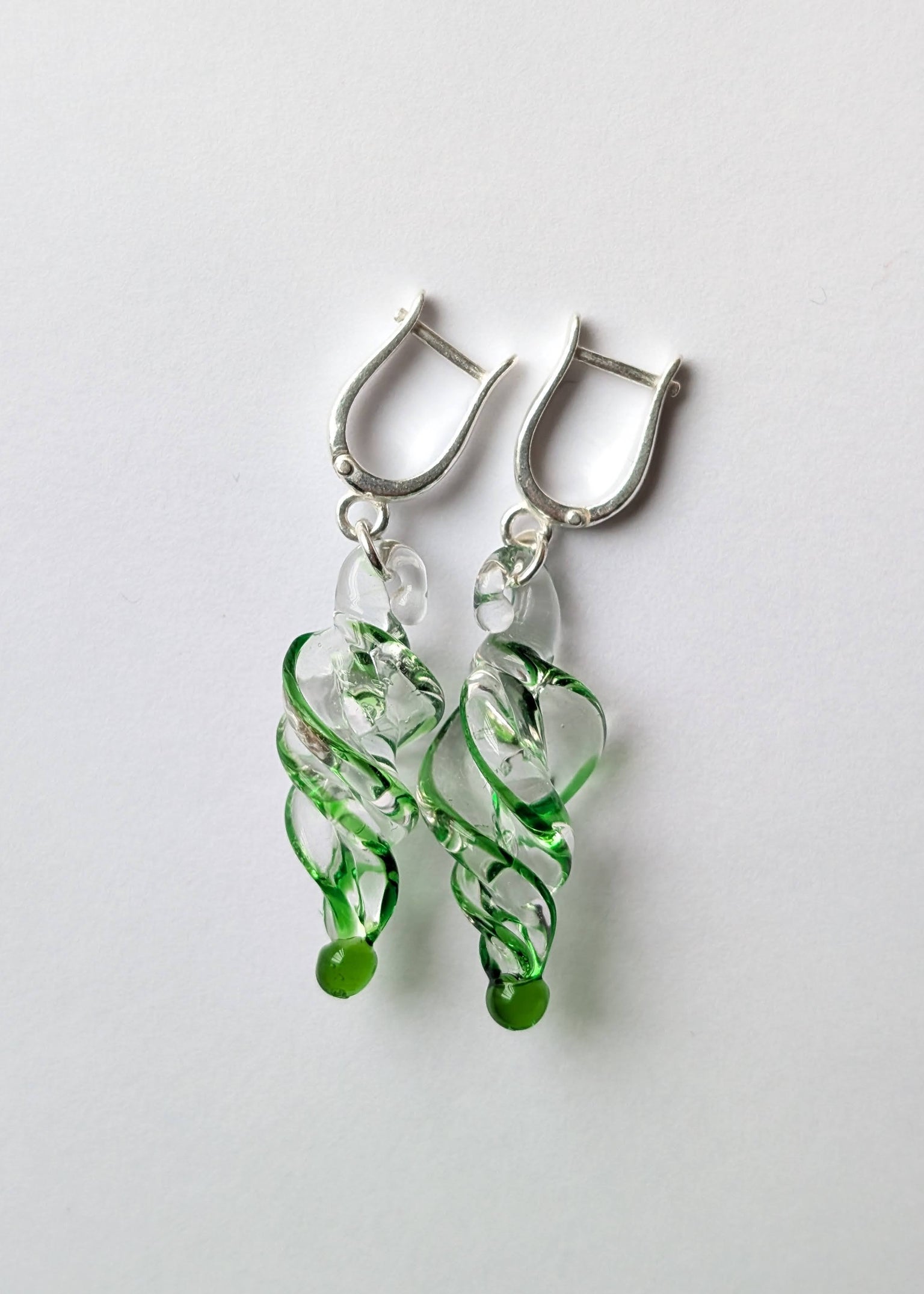 Green and silver earrings on a light gray background