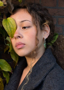 Woman with green earrings standing next to a plant
