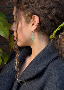 Close-up of a person wearing green earrings with a blurred natural background