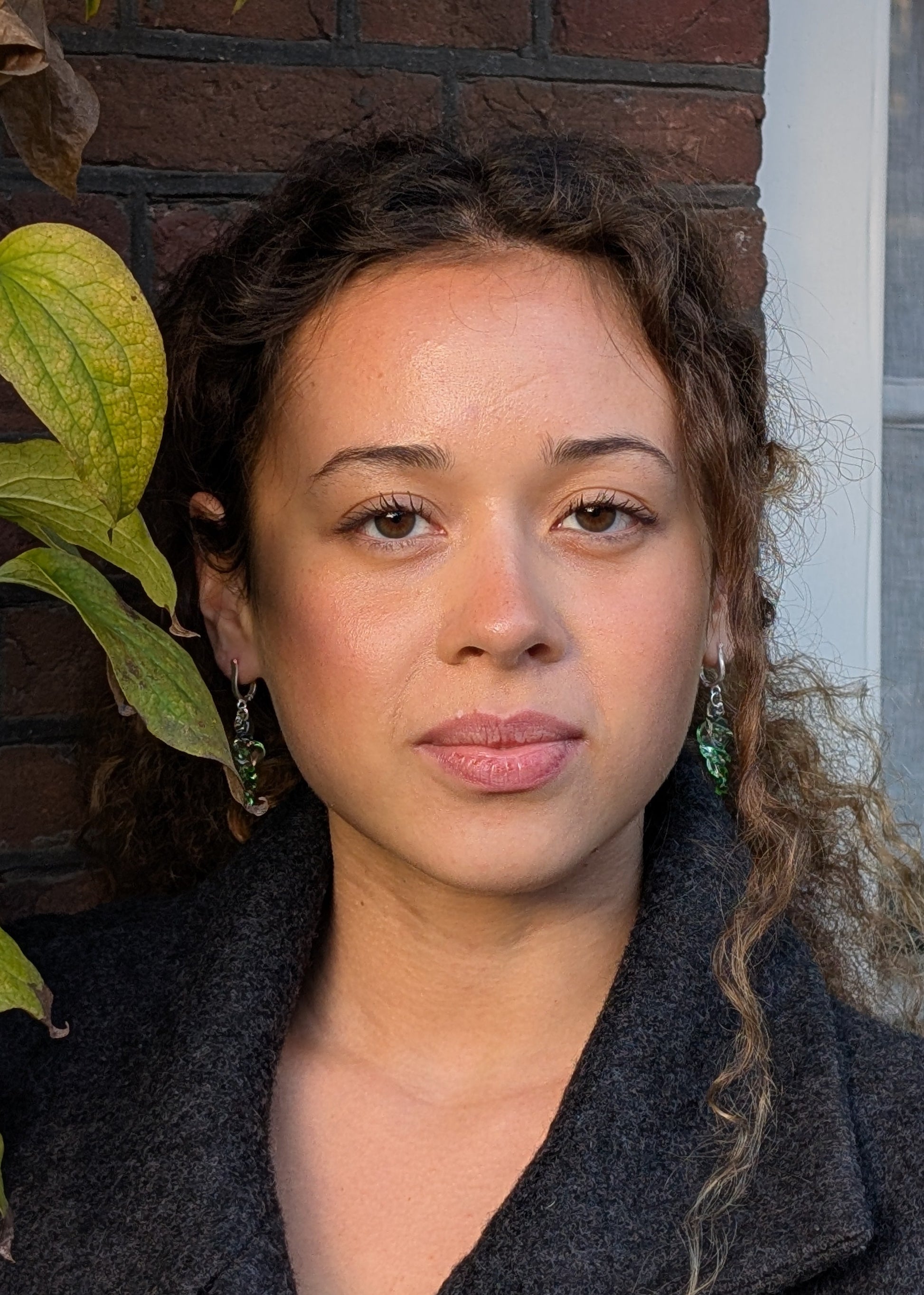 Woman standing outdoors with a plant and brick wall in the background