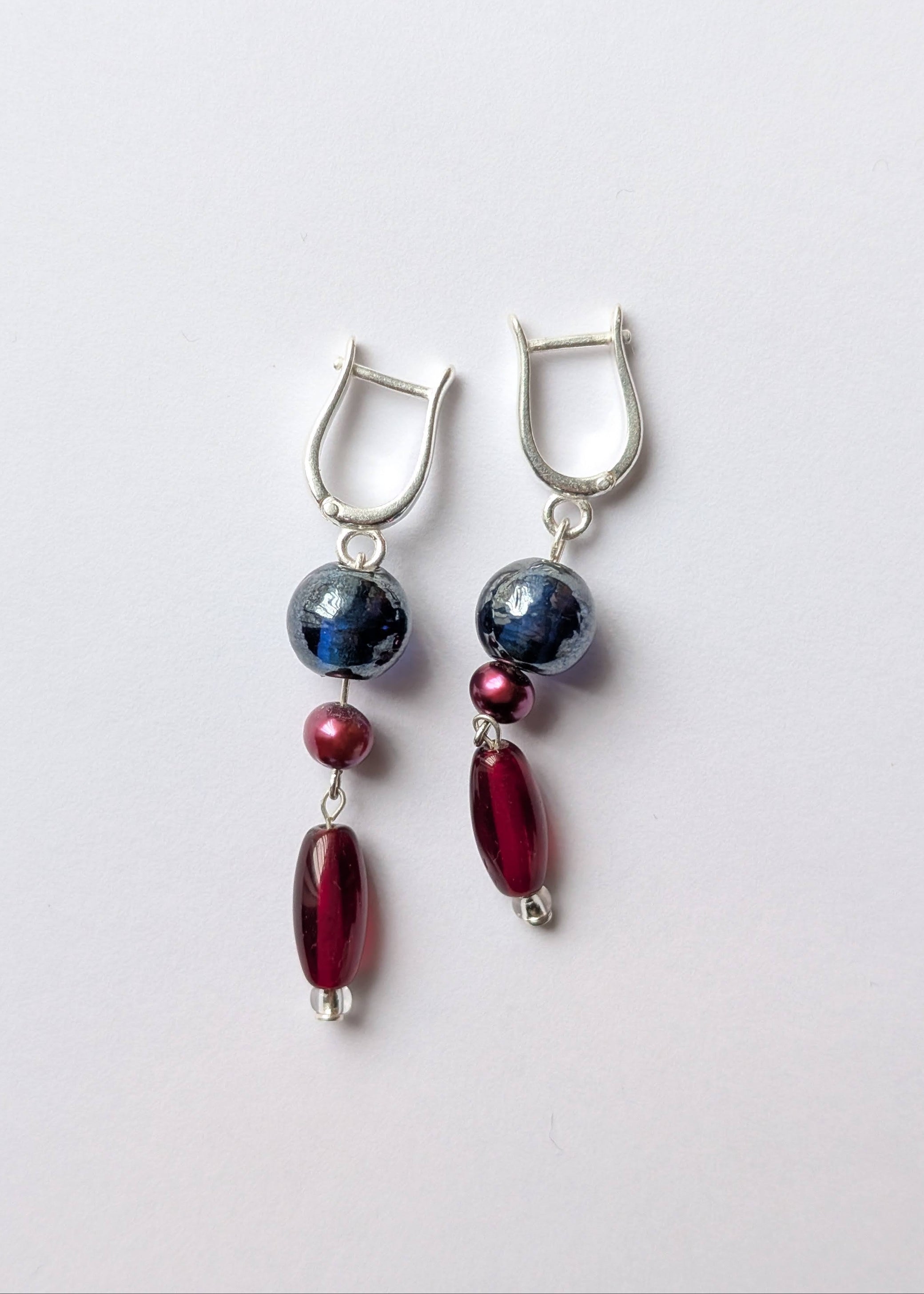 Pair of earrings with blue, red, and silver beads on a light gray background