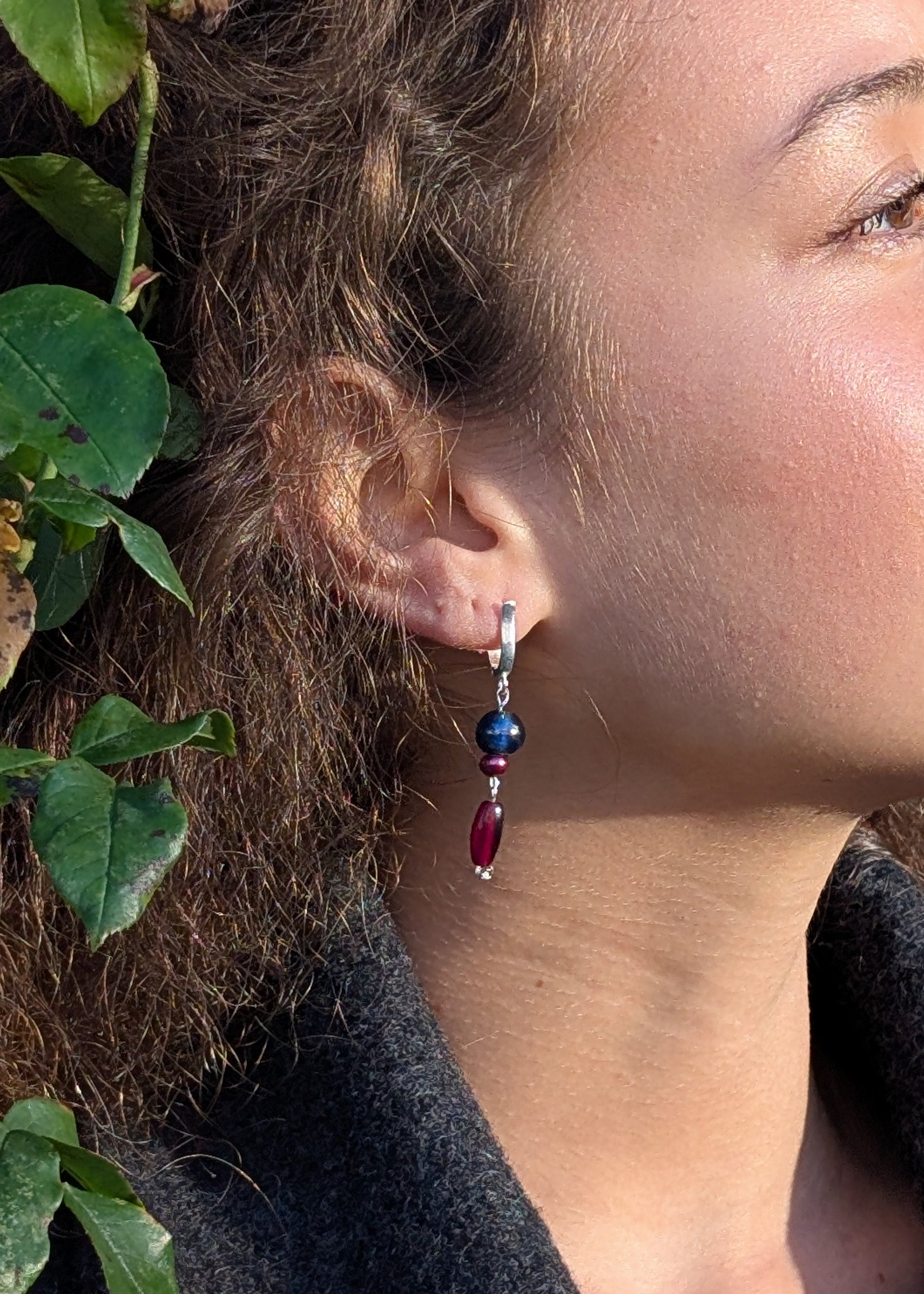 Close-up of a person wearing colorful earrings with leaves in the background