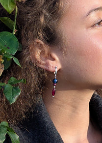 Close-up of a person wearing colorful earrings with leaves in the background
