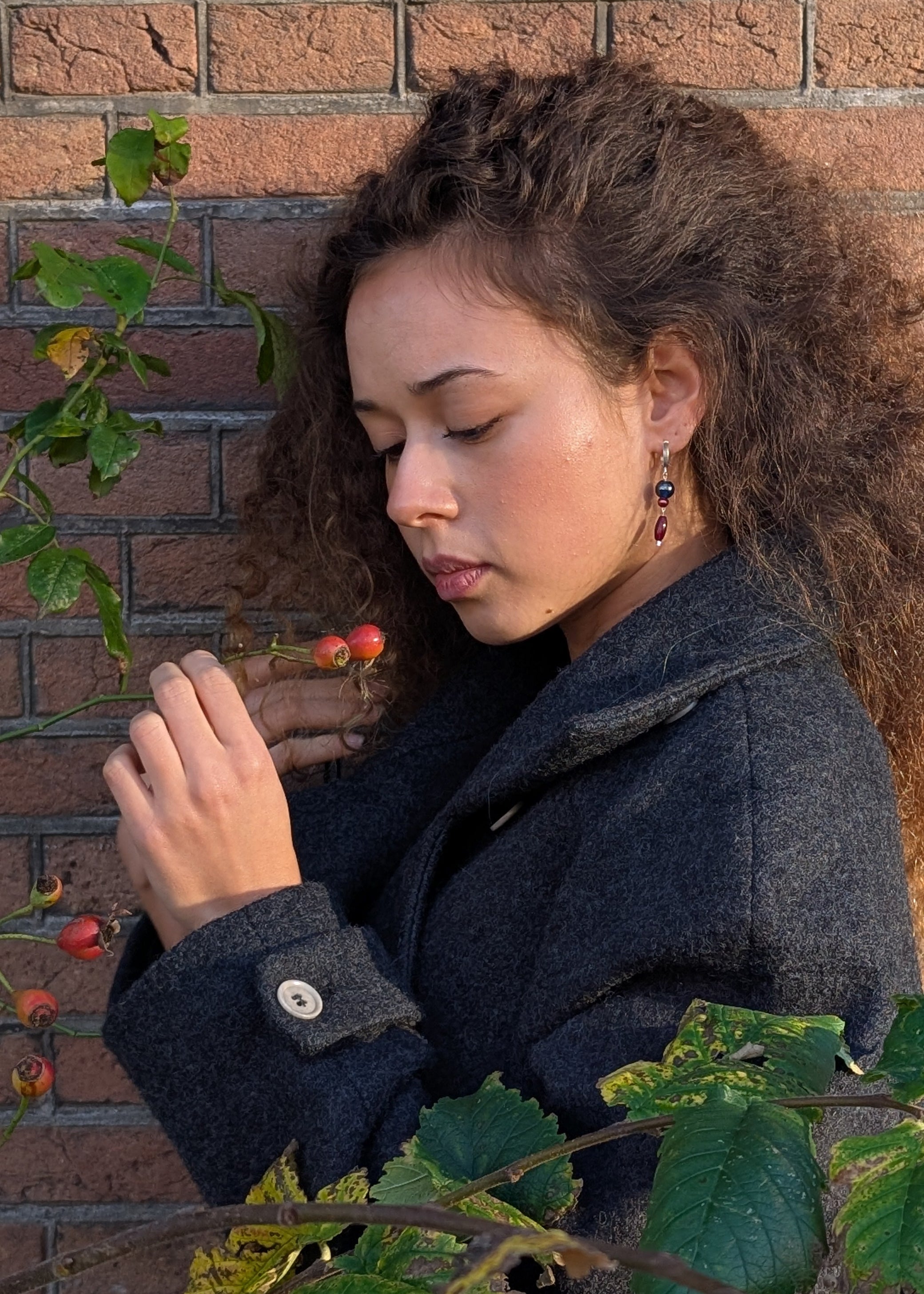 Woman holding a berry against a brick wall with leaves