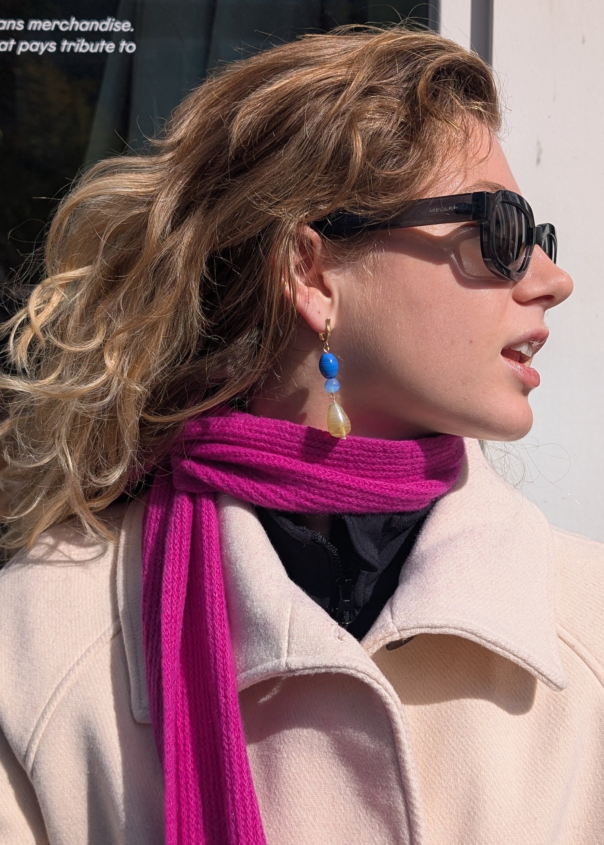 Woman wearing sunglasses and a bright pink scarf with a beige coat.