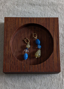 Pair of earrings with blue and yellow stones in a wooden display box on a gray background