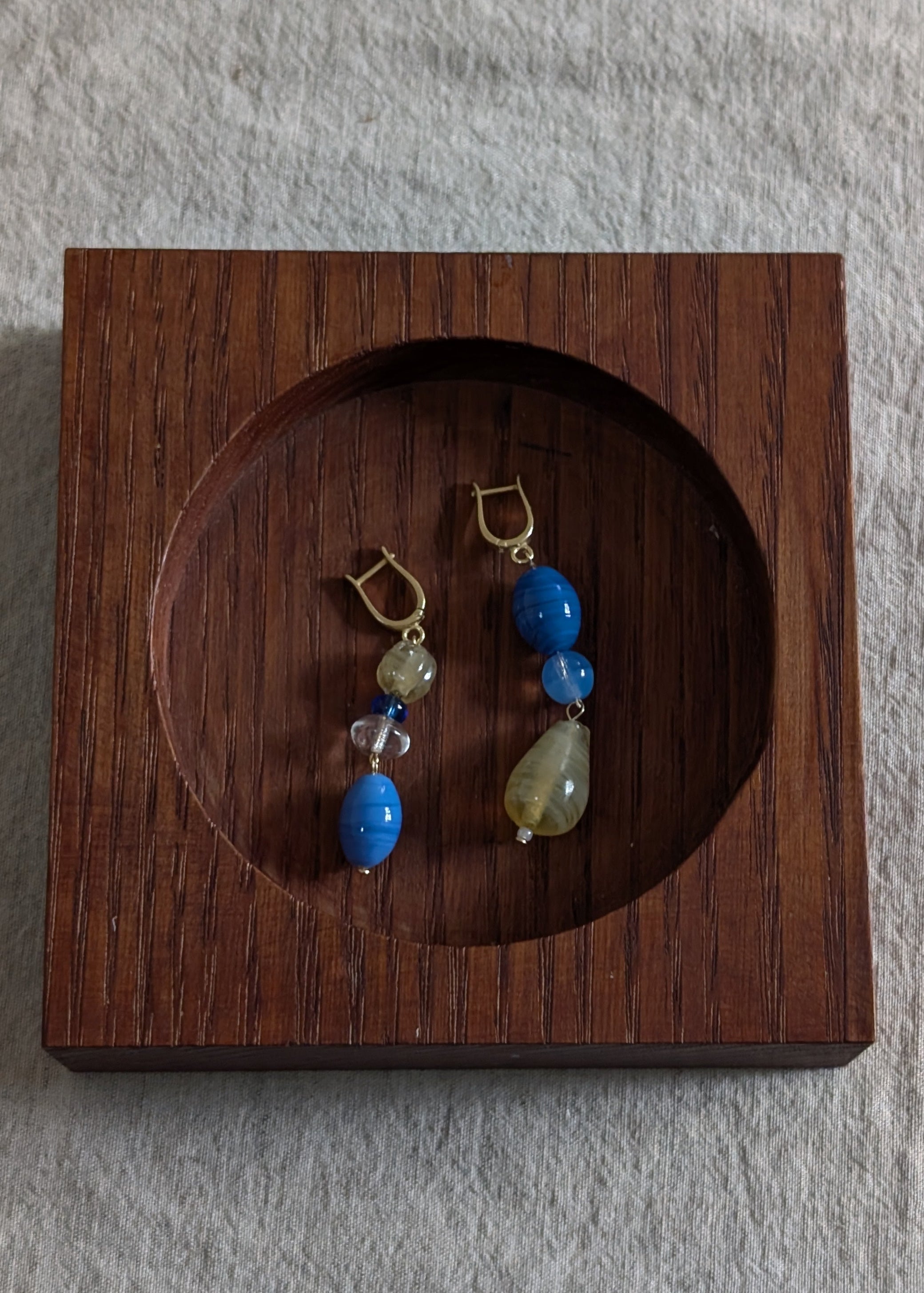 Pair of earrings with blue and yellow stones in a wooden display box on a gray background