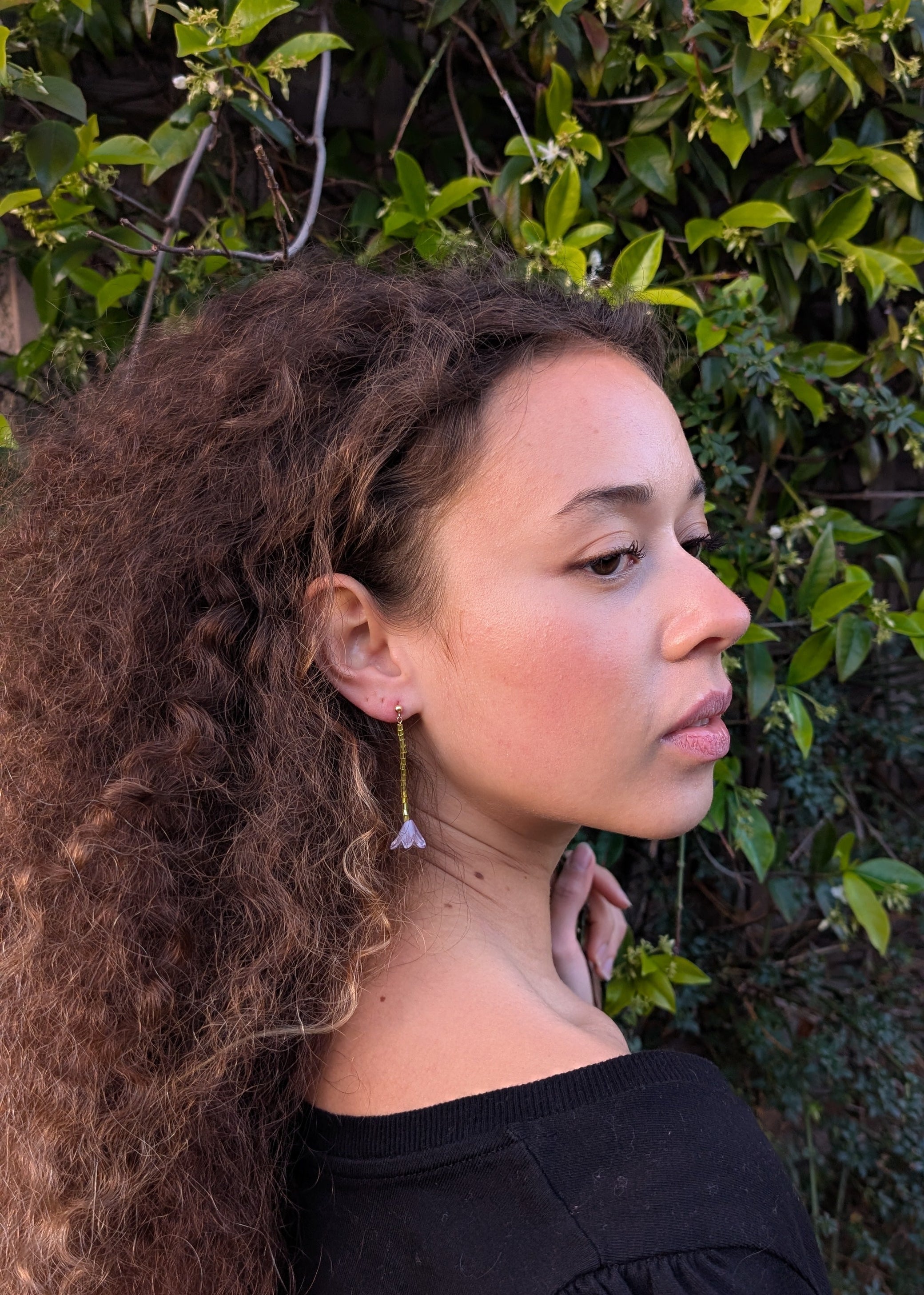 Woman with long curly hair standing in front of green foliage