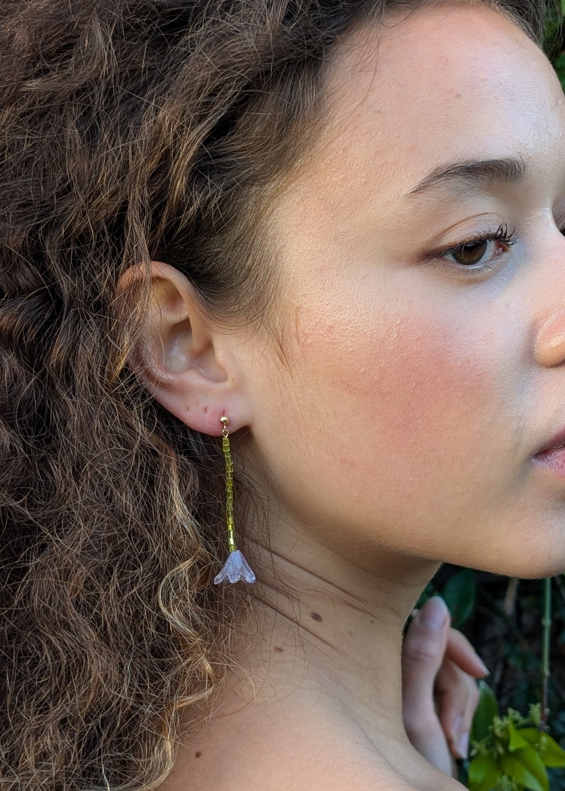 Close-up of a person wearing earrings with a blurred natural background