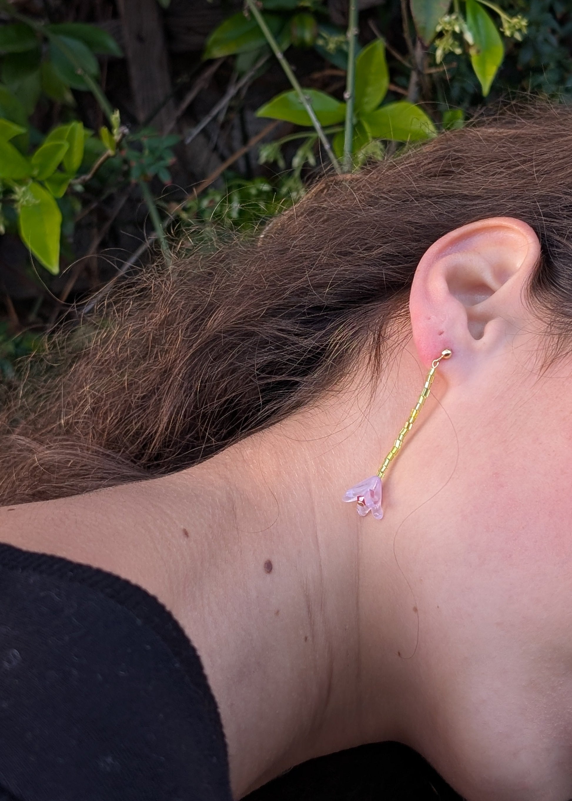Close-up of an ear wearing a floral earring with a green leafy background