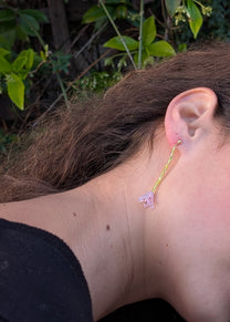 Close-up of an ear wearing a floral earring with a green leafy background