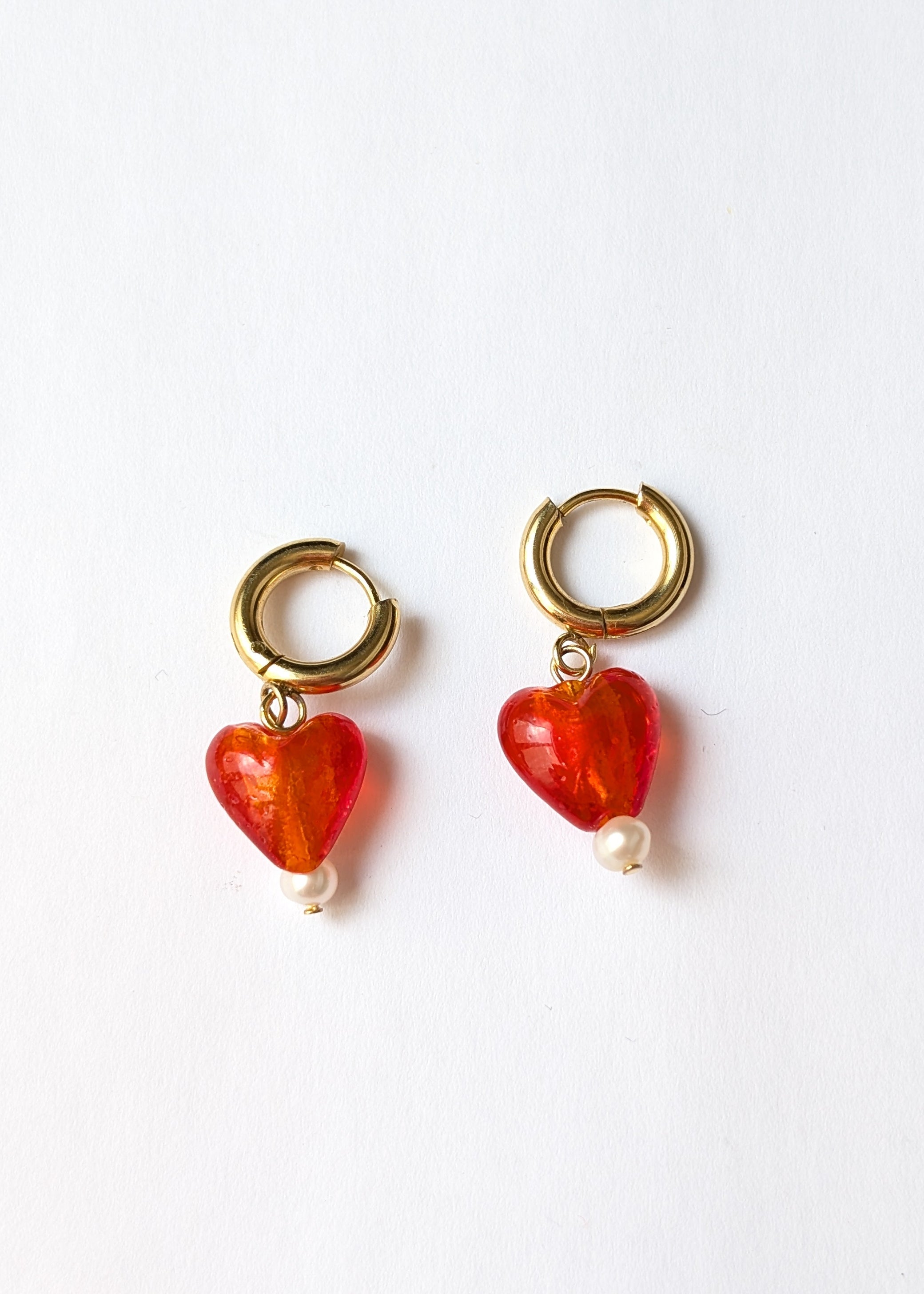 Pair of earrings with red heart-shaped charms and gold hooks on a white background
