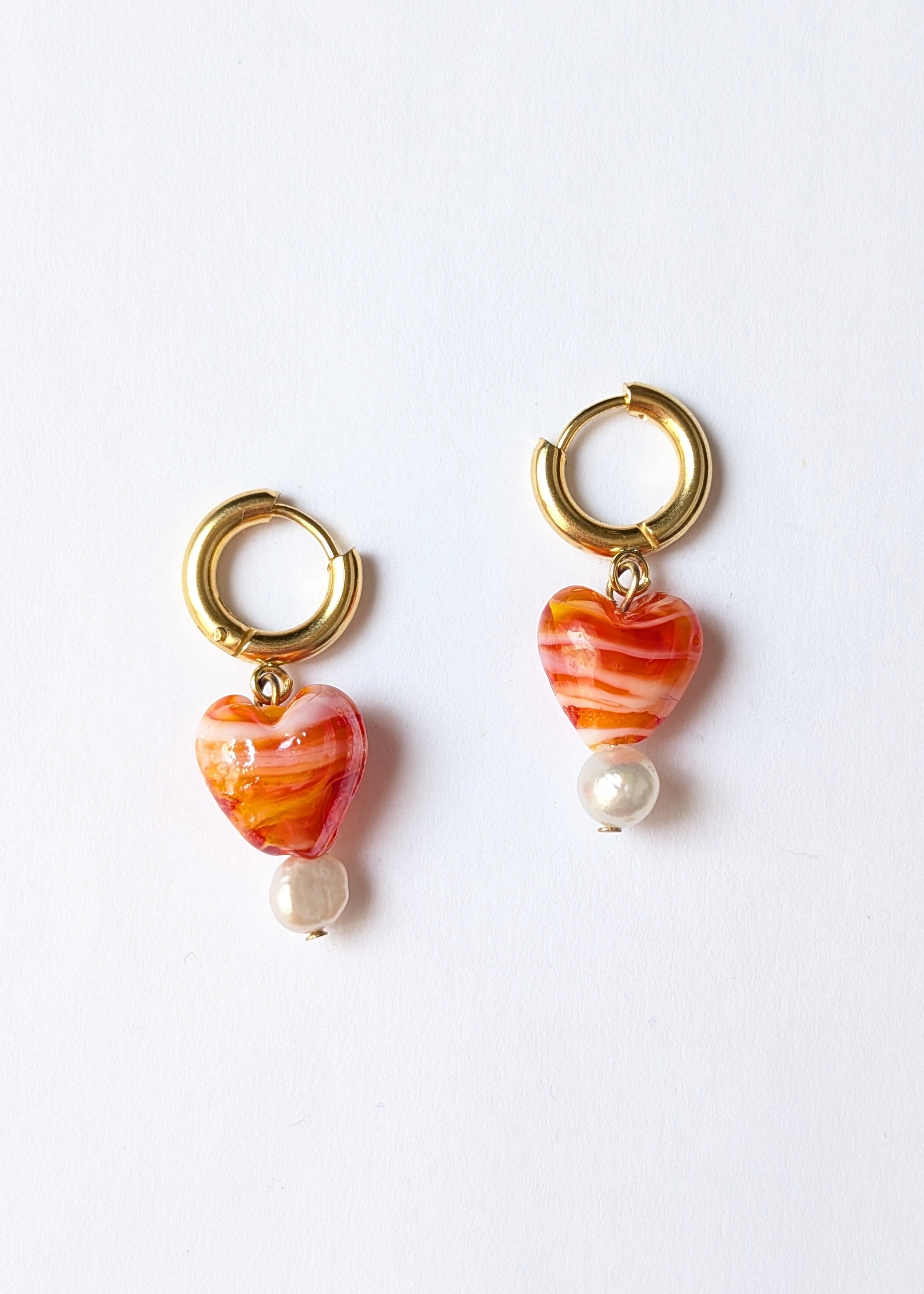 Pair of earrings with gold loops, orange and white beads on a white background