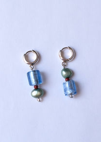Pair of earrings with blue and green beads on a light purple background