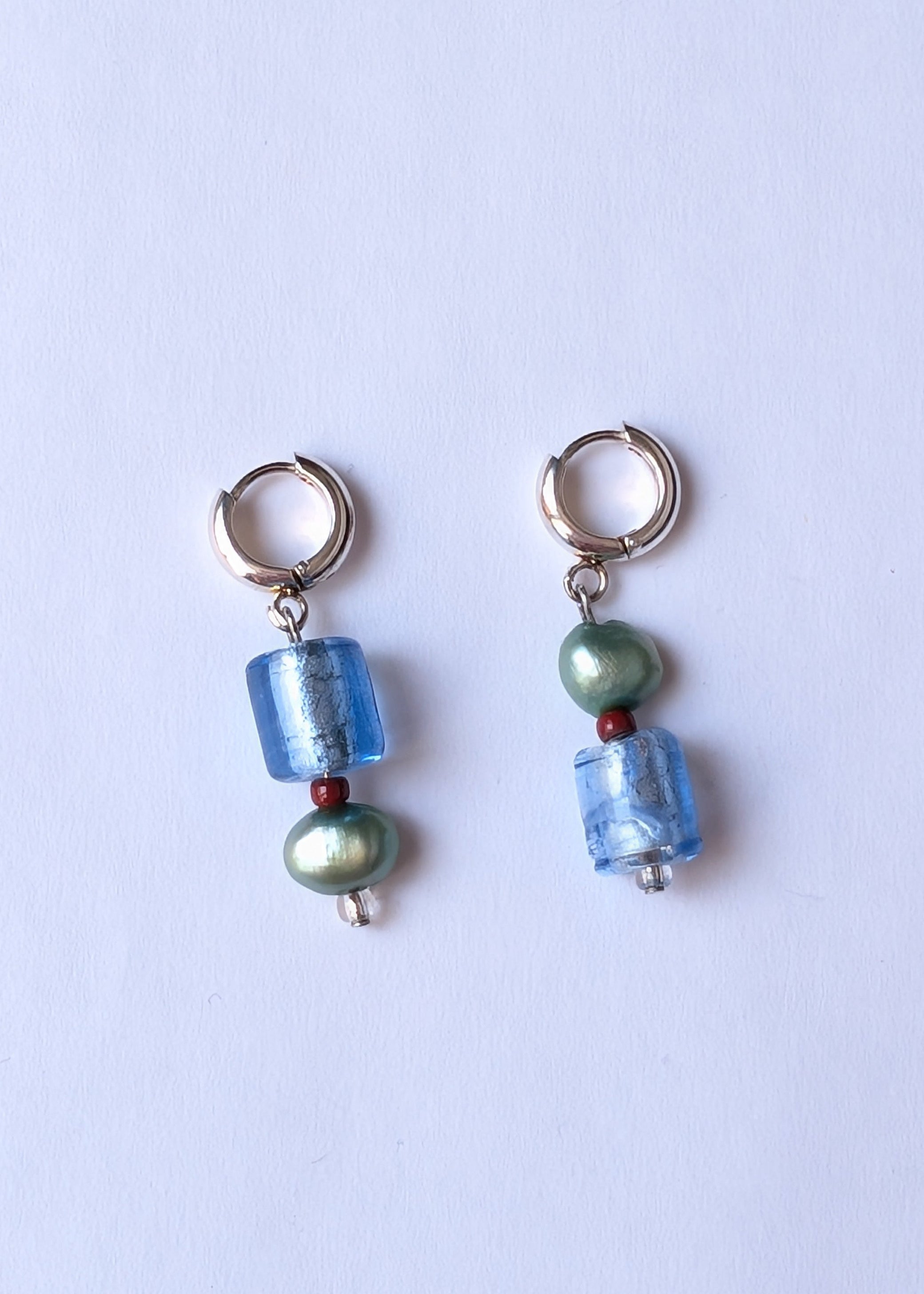 Pair of earrings with blue and green beads on a light purple background