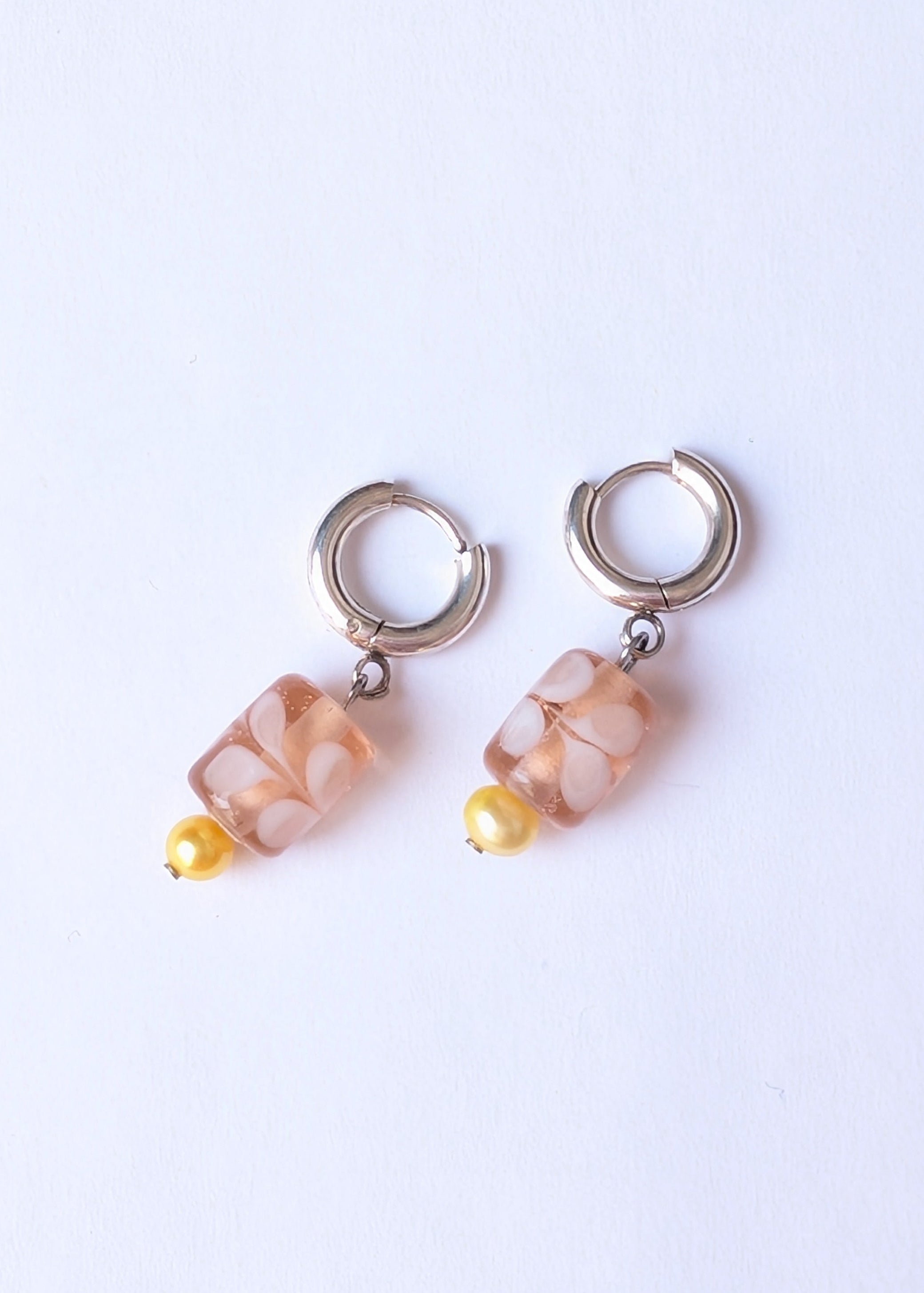 Pair of hoop earrings with beige stone beads on a light purple background