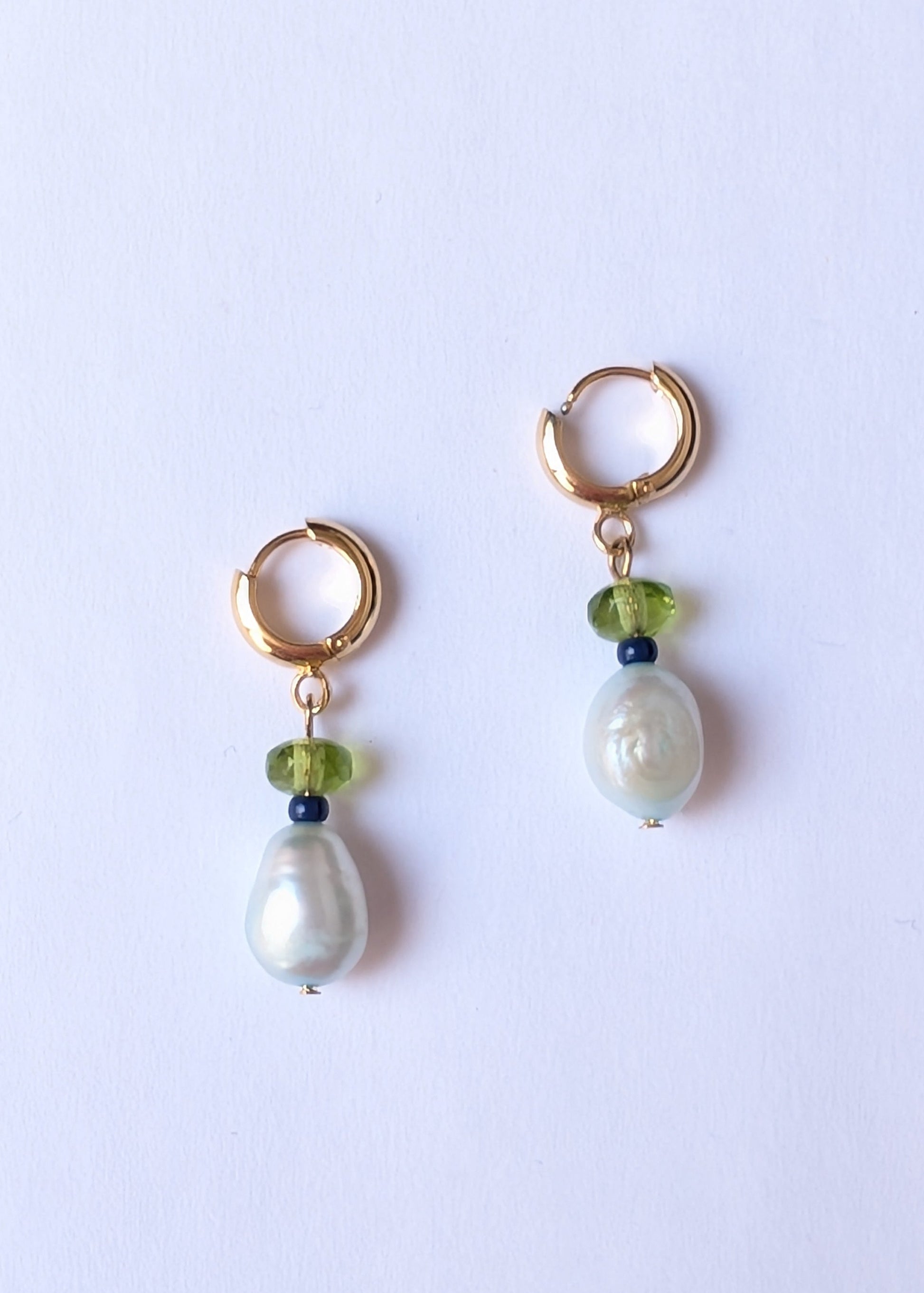 Pair of gold hoop earrings with pearl and green bead drops on a light purple background
