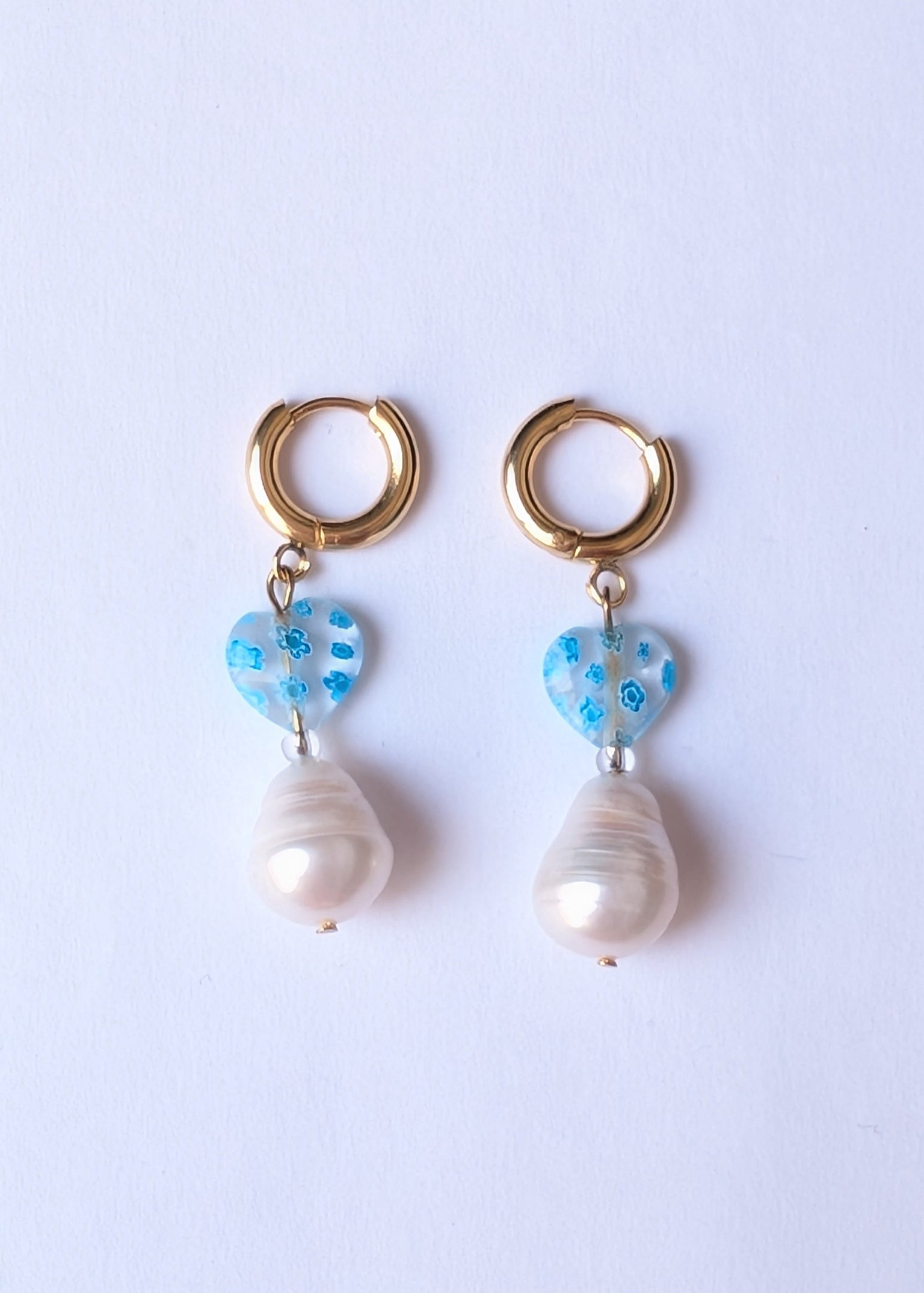 Pair of earrings with pearl drops and blue heart-shaped charms on a light purple background