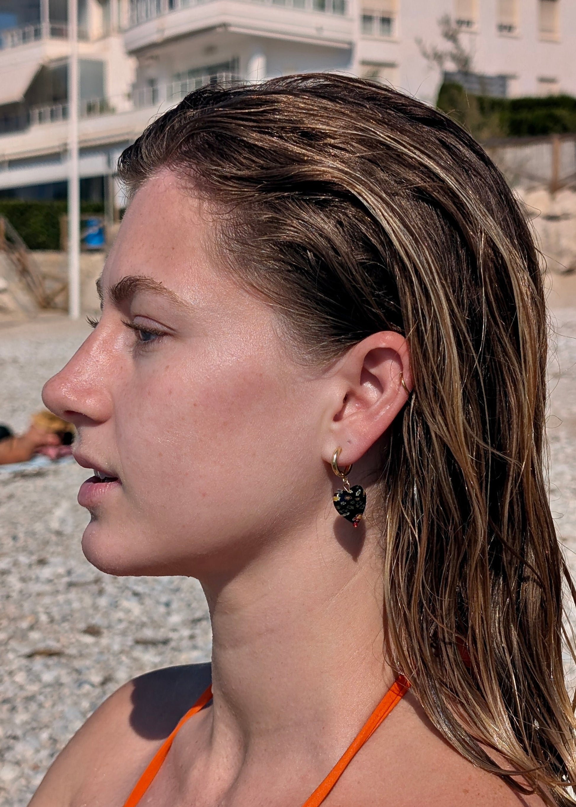 Woman with wet hair on a beach, wearing an orange bikini top.