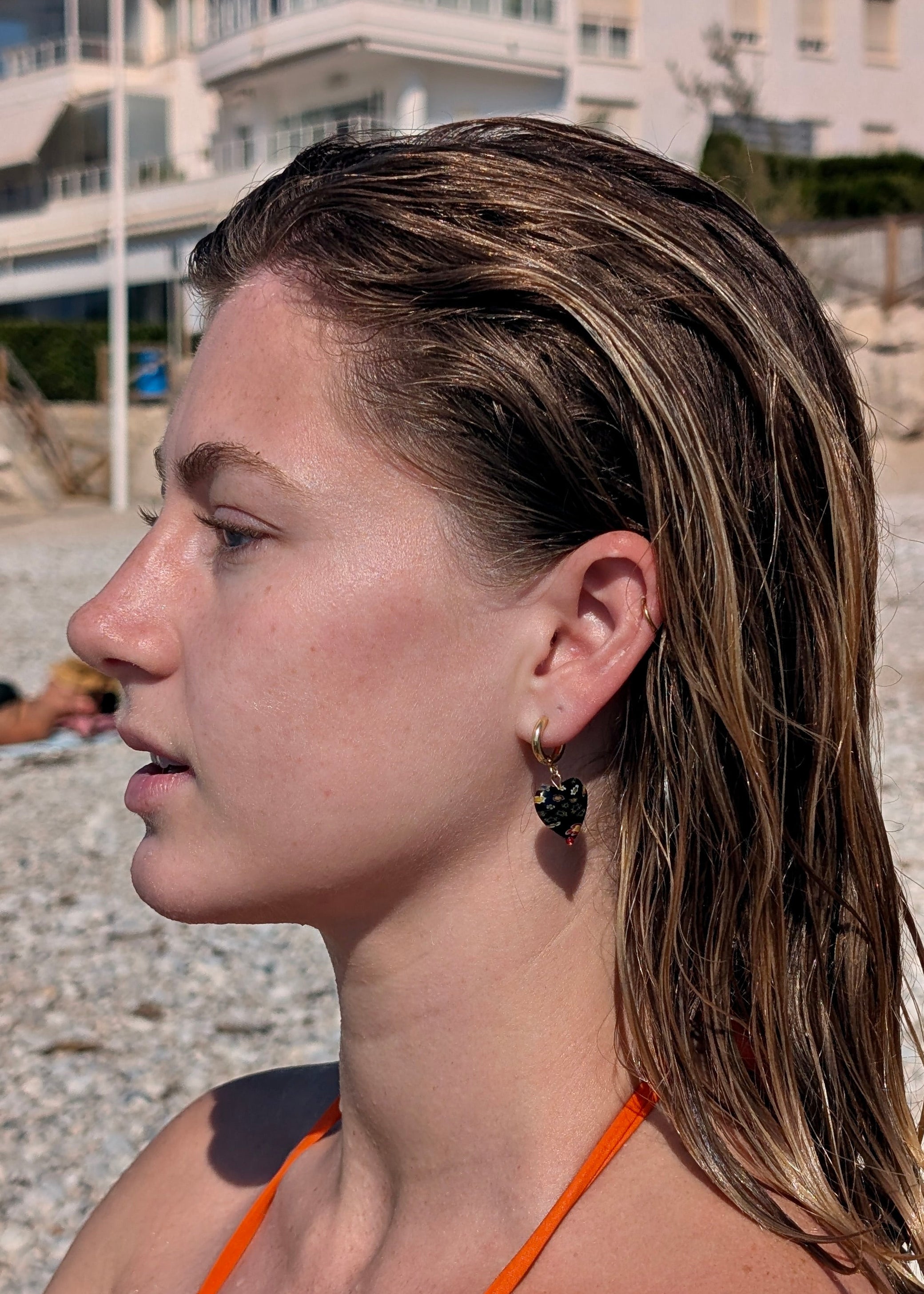 Woman with wet hair on a beach, wearing an orange bikini top.