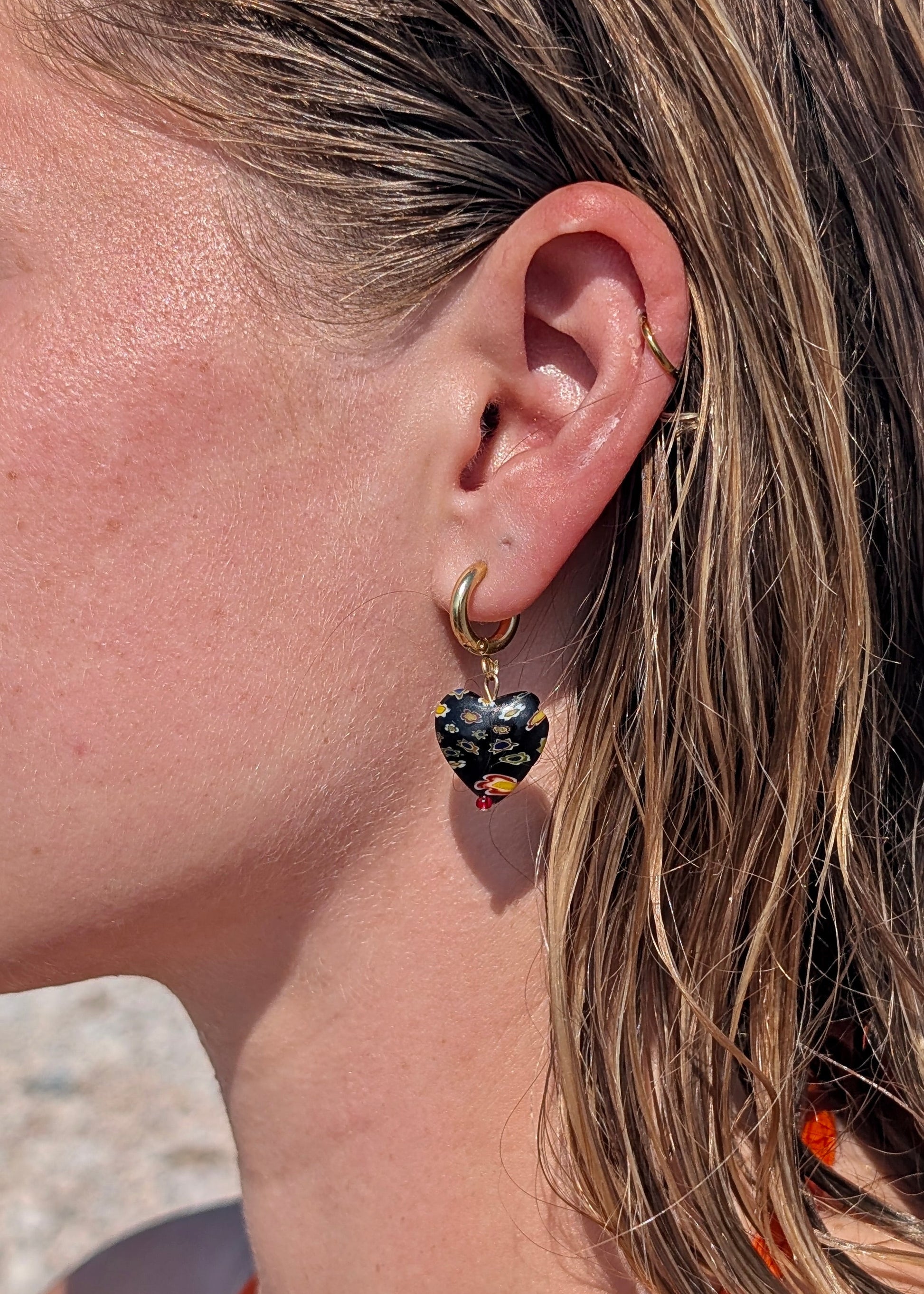 Close-up of a person wearing a hoop earring with a dark heart-shaped gemstone.