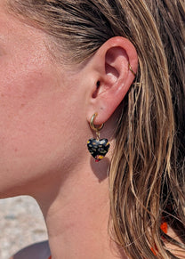 Close-up of a person wearing a hoop earring with a dark heart-shaped gemstone.