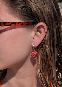 Close-up of a person wearing a red floral earring with a blurred background