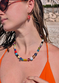 Woman wearing a colorful beaded necklace and orange top with sunglasses, outdoors.