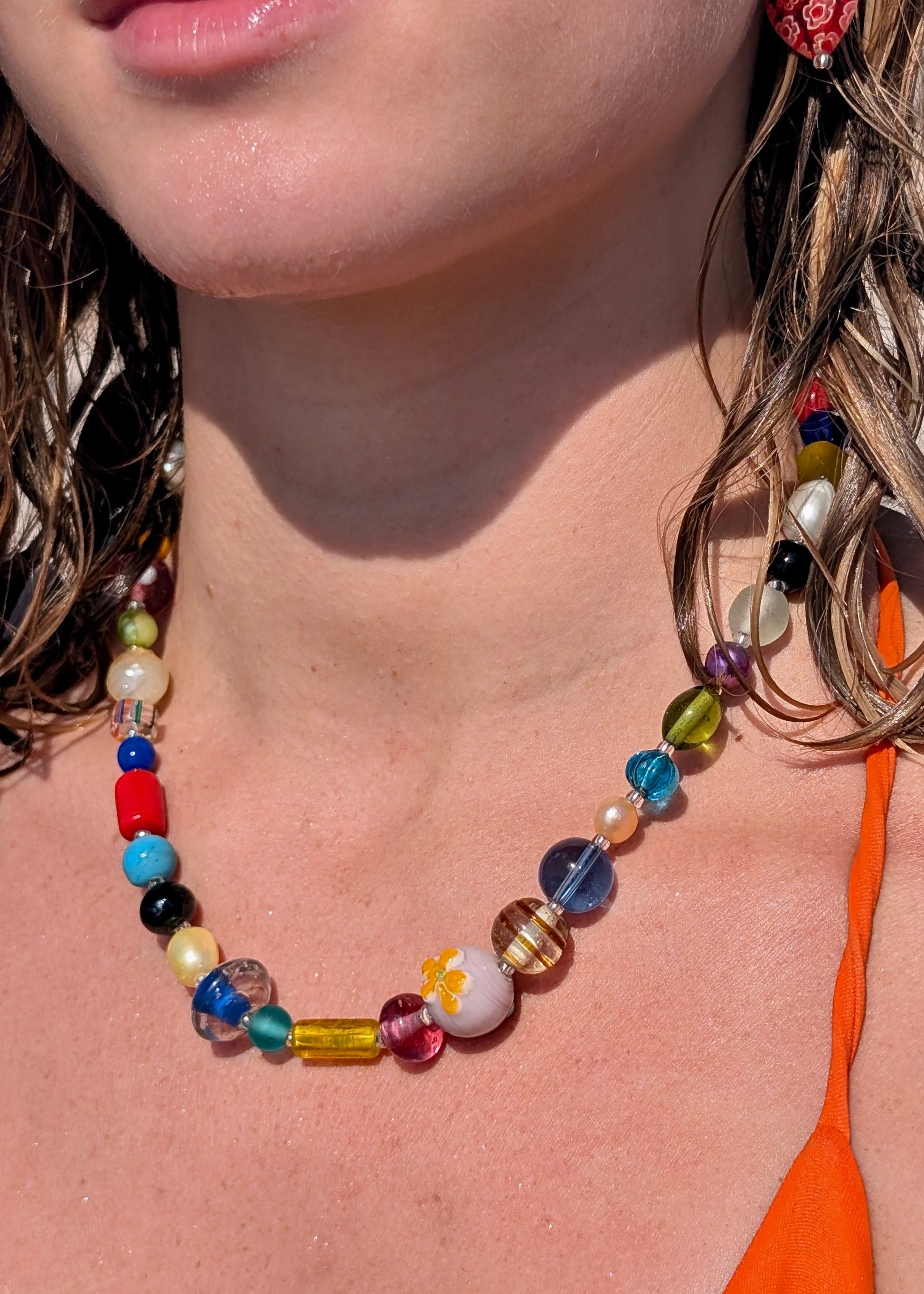 Close-up of a colorful beaded necklace and earrings on a person with an orange top.