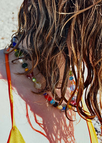 Close-up of a person with wet hair wearing a colorful beaded necklace against a neutral background