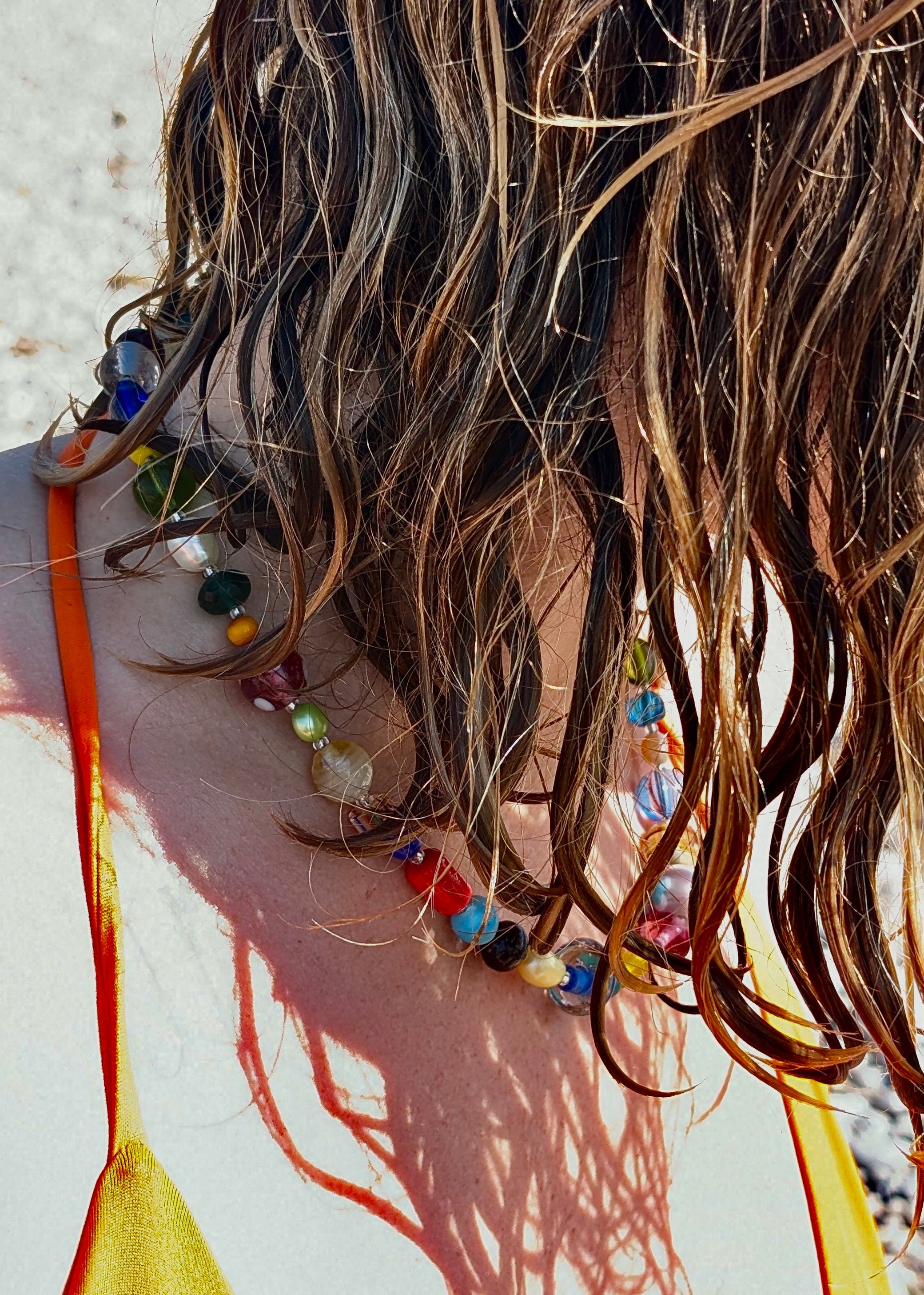 Close-up of a person with wet hair wearing a colorful beaded necklace against a neutral background