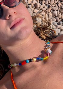 Woman wearing sunglasses and a colorful beaded necklace lying on pebbles.