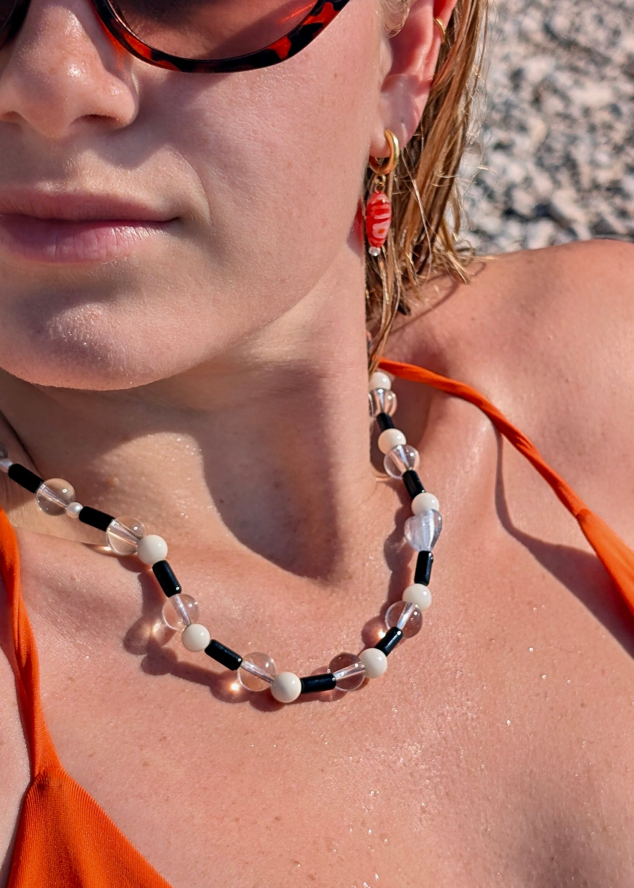 Close-up of a person wearing an orange top and a beaded necklace with a blurred background