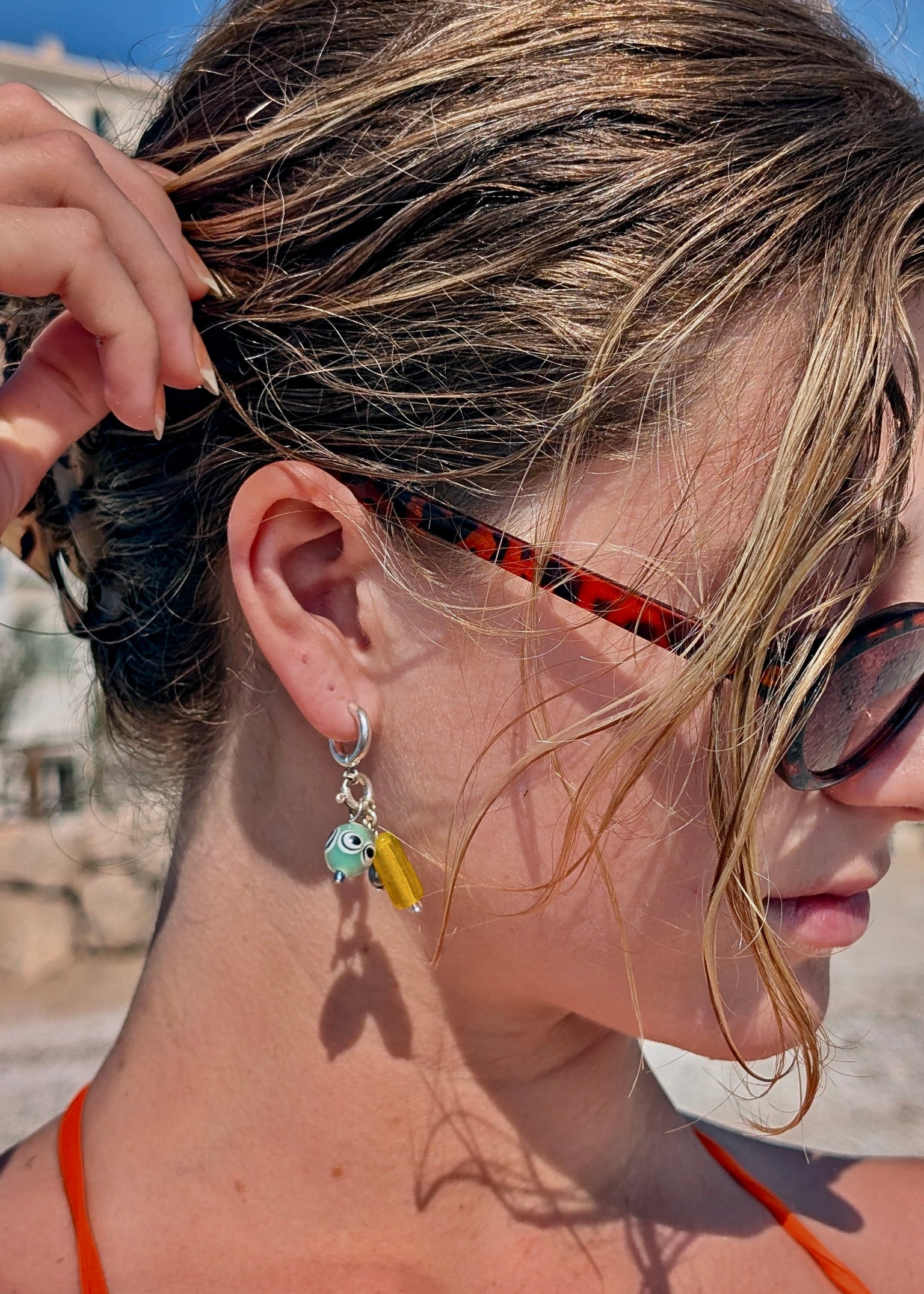Close-up of a person with sunglasses and earrings, outdoors.