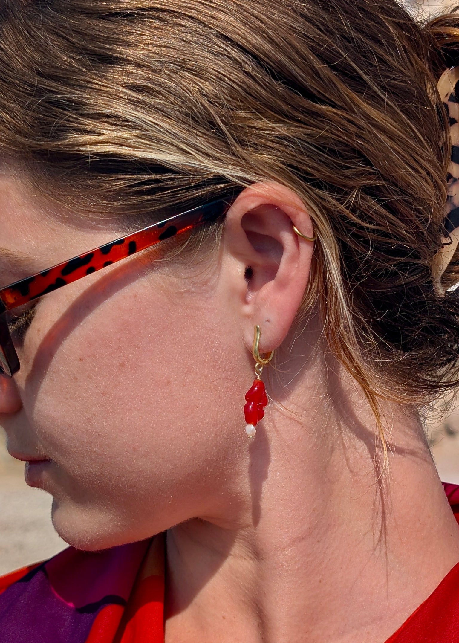Close-up of a person wearing red earrings and sunglasses with a blurred background