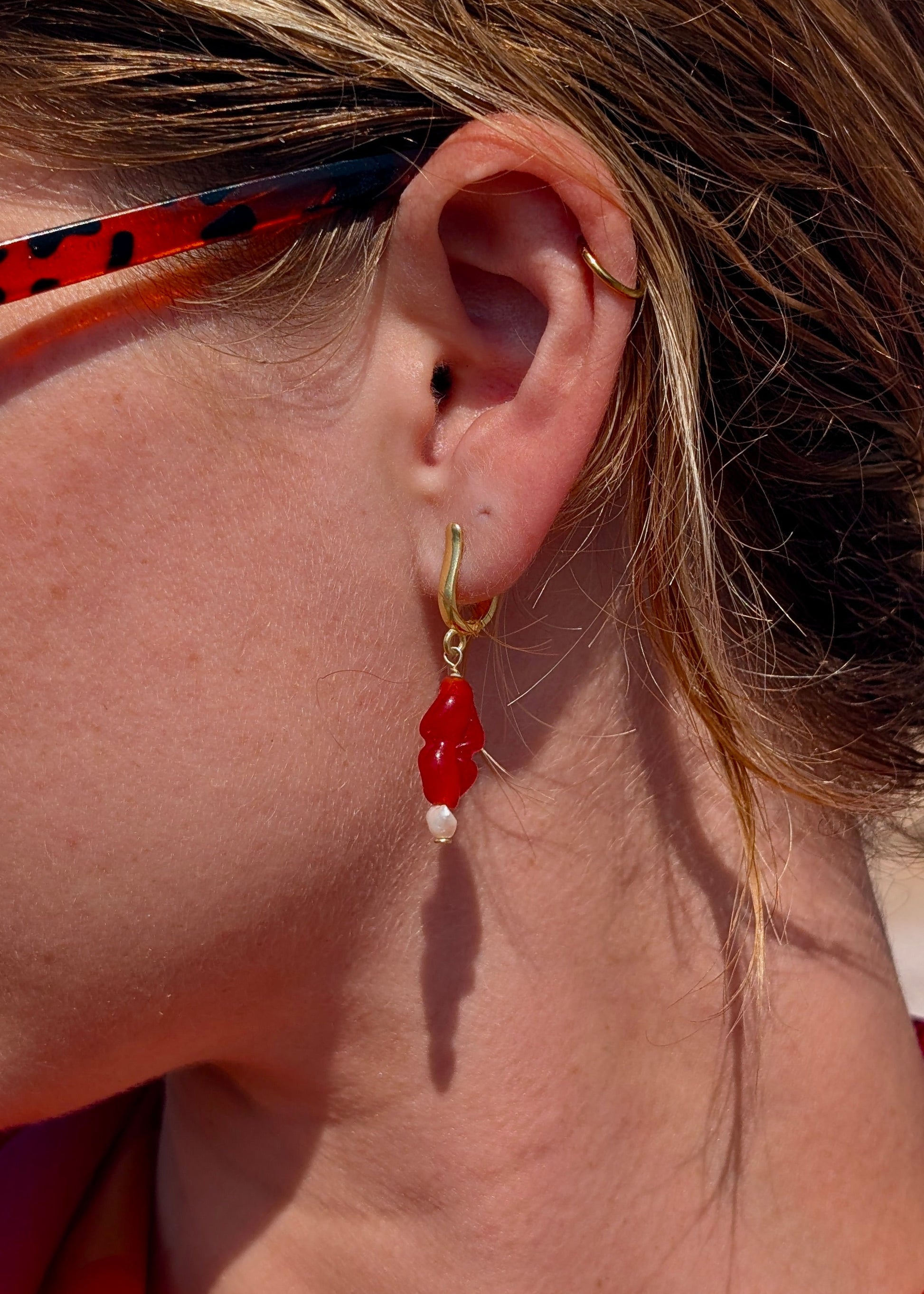 Close-up of a person wearing a red earring with a gold hoop.